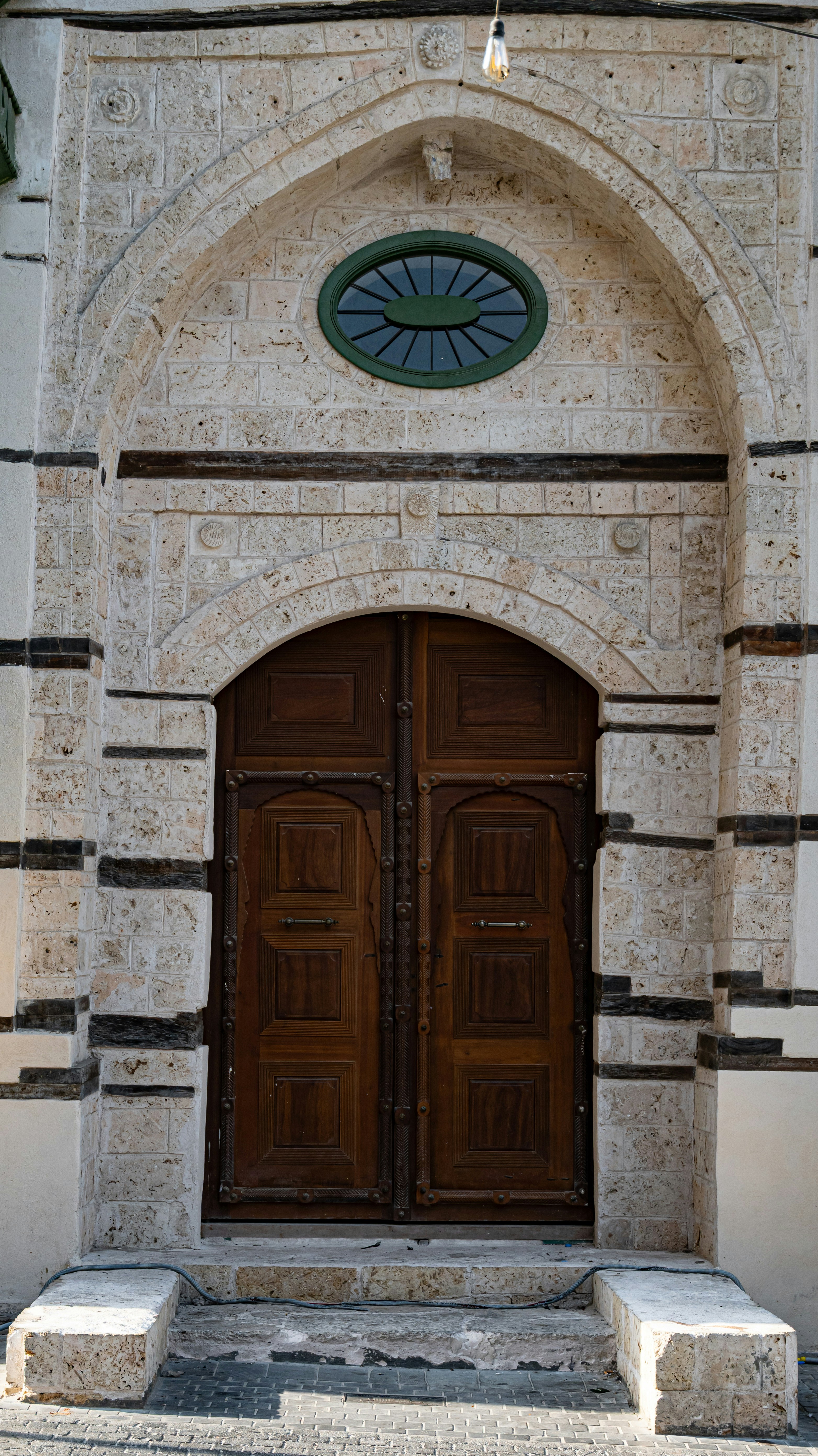 An arched wooden double door set into a textured stone wall with dark horizontal accents