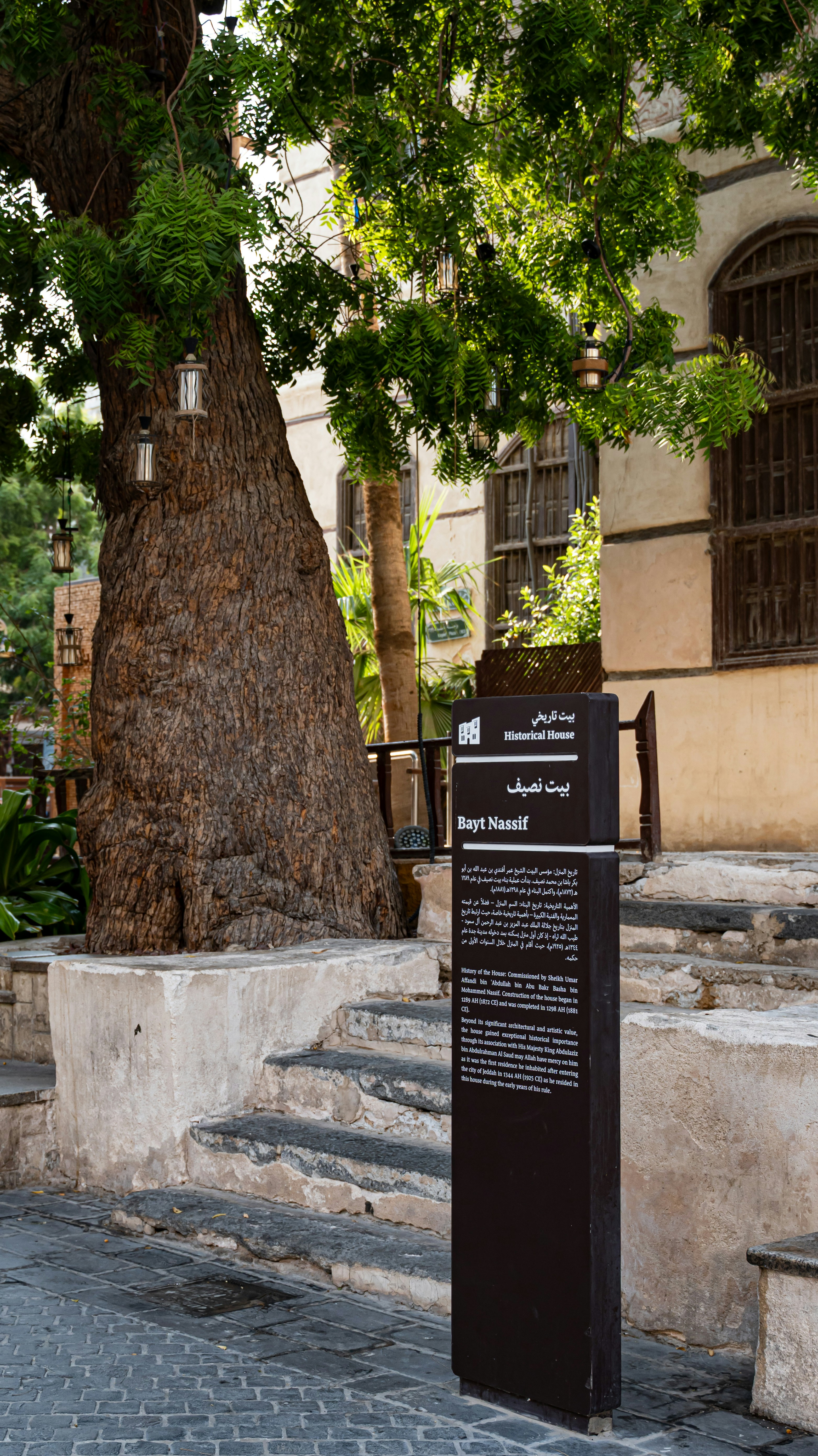 A sign for Bayt Nassif in front of a large tree and historic building