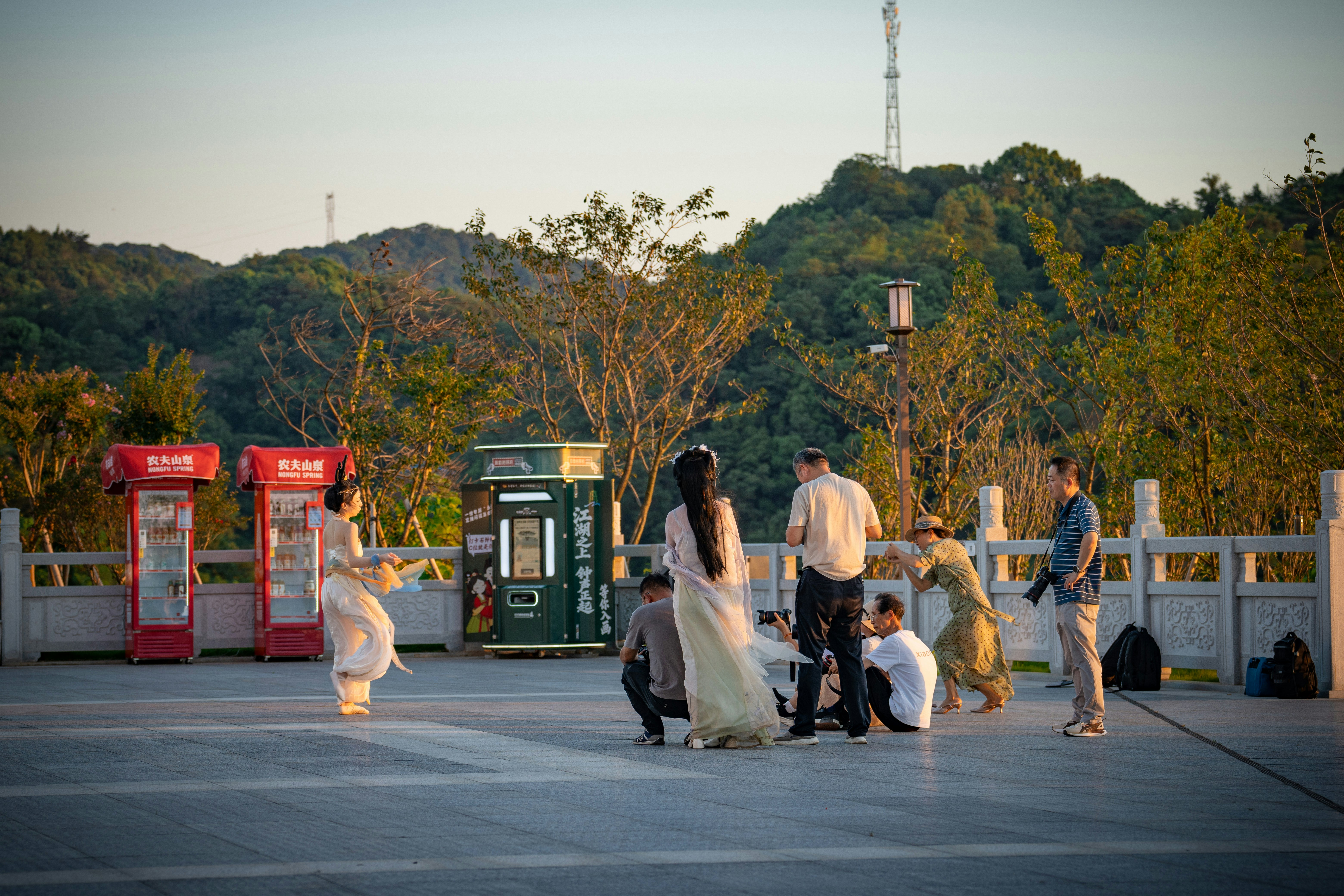 A woman in traditional dress dancing for photographers on a paved plaza at dusk