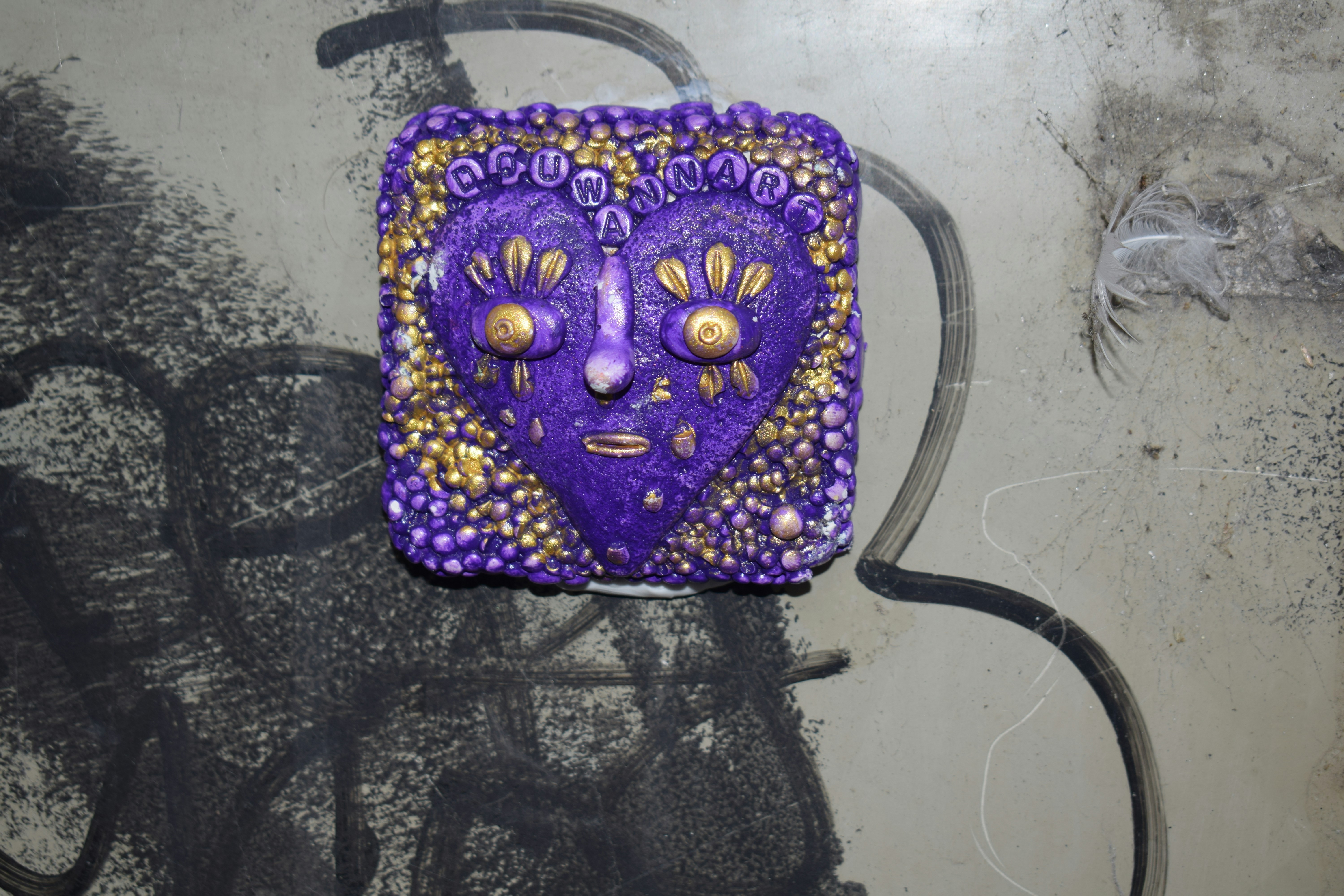 A purple heart-shaped sculpture with gold accents on a surface with black graffiti