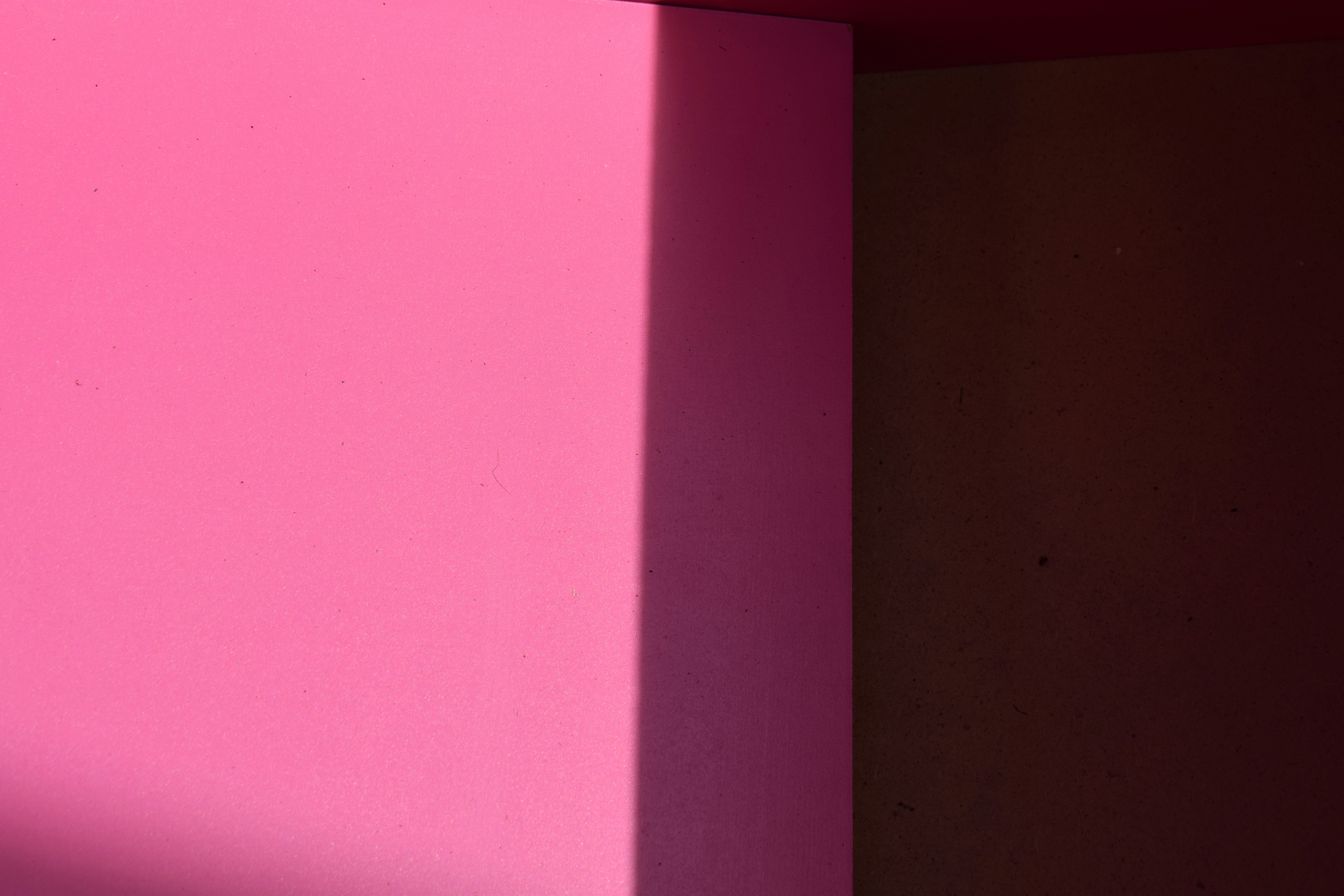 A bright pink surface beside a dark brown shadow on a flat plane