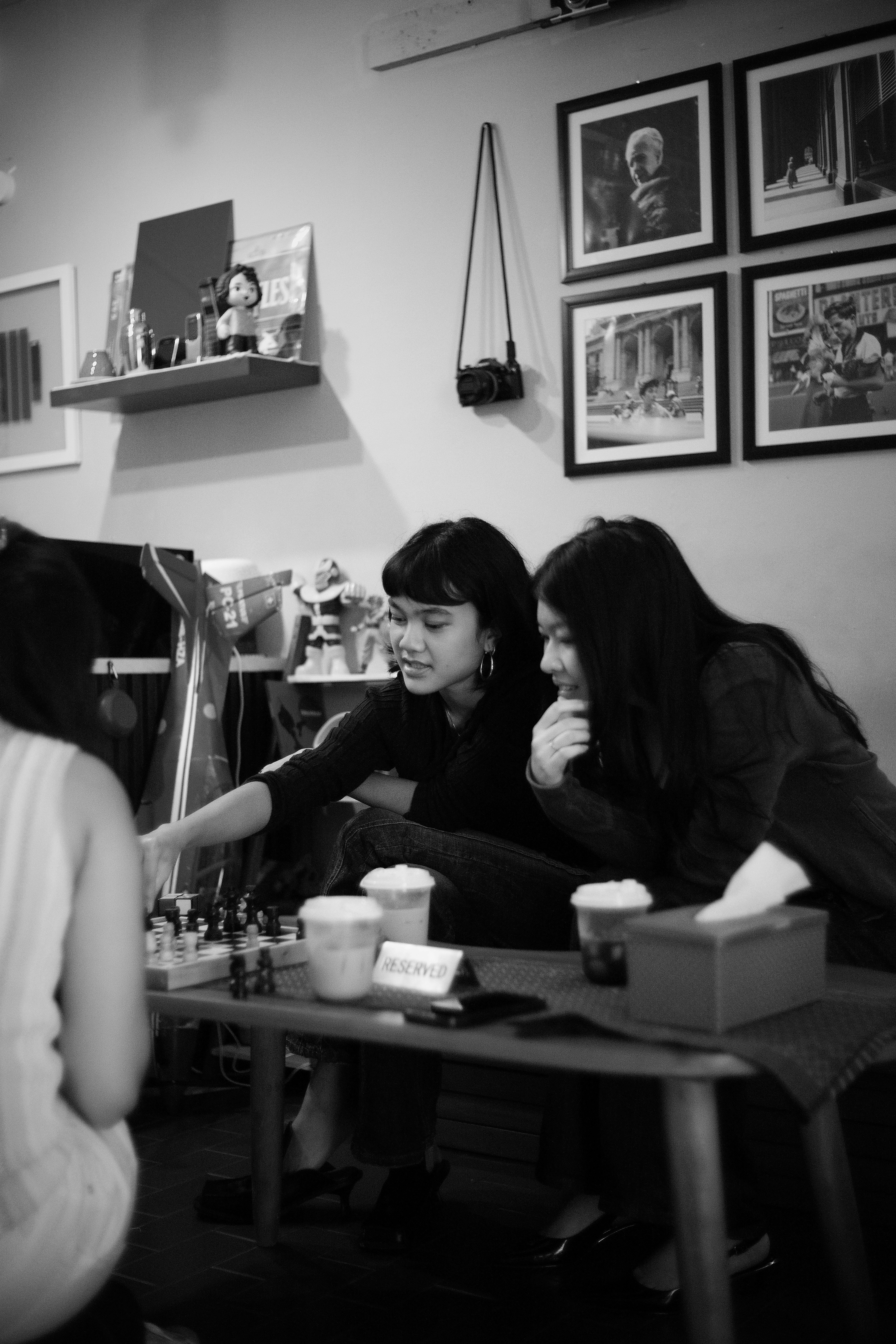 Três pessoas jogando xadrez em uma mesa com bebidas em um café
