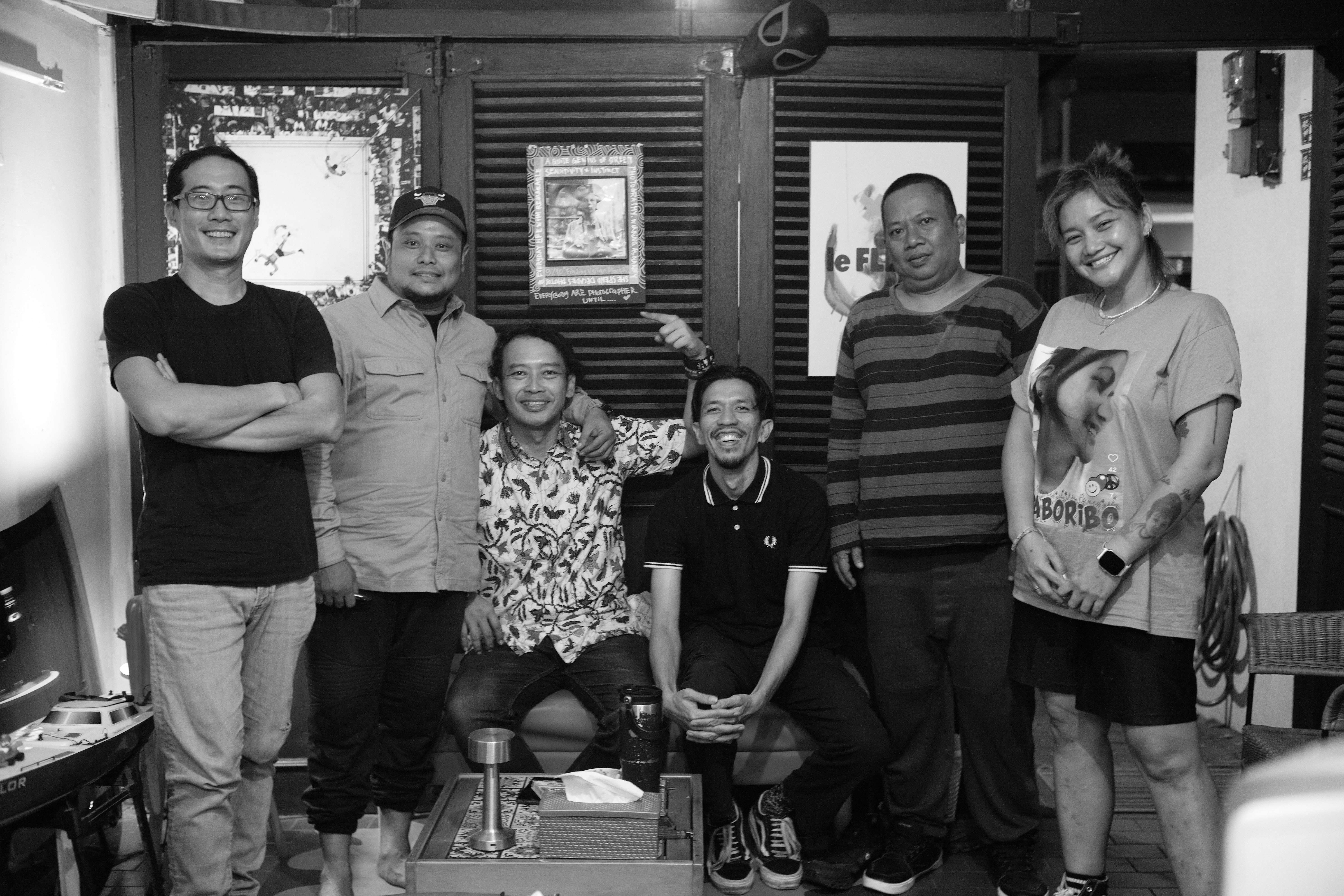 壁にポスターが貼られた部屋で6人が一緒にポーズをとっているグループ