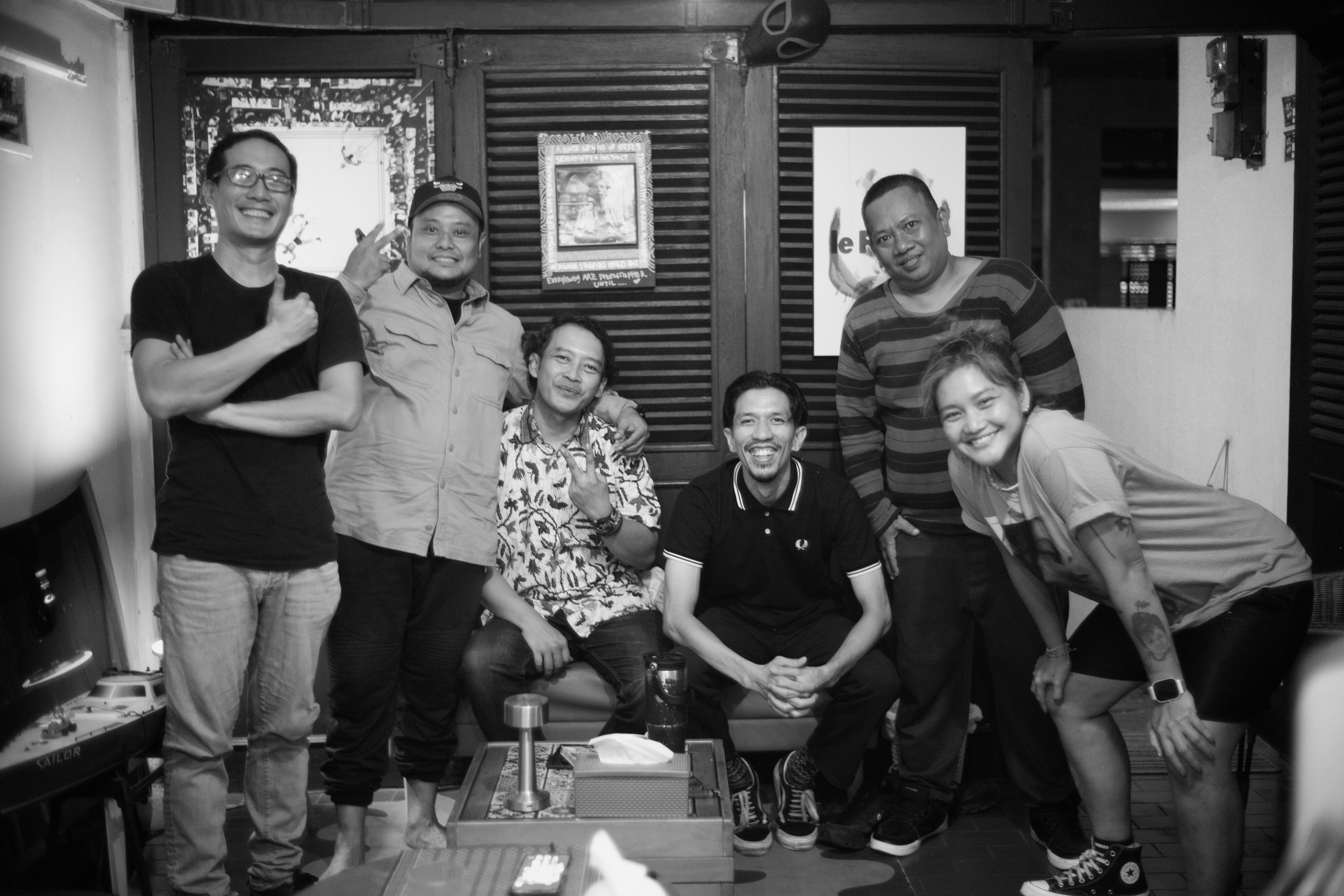 A group of six adults posing together in a room with wooden shutters