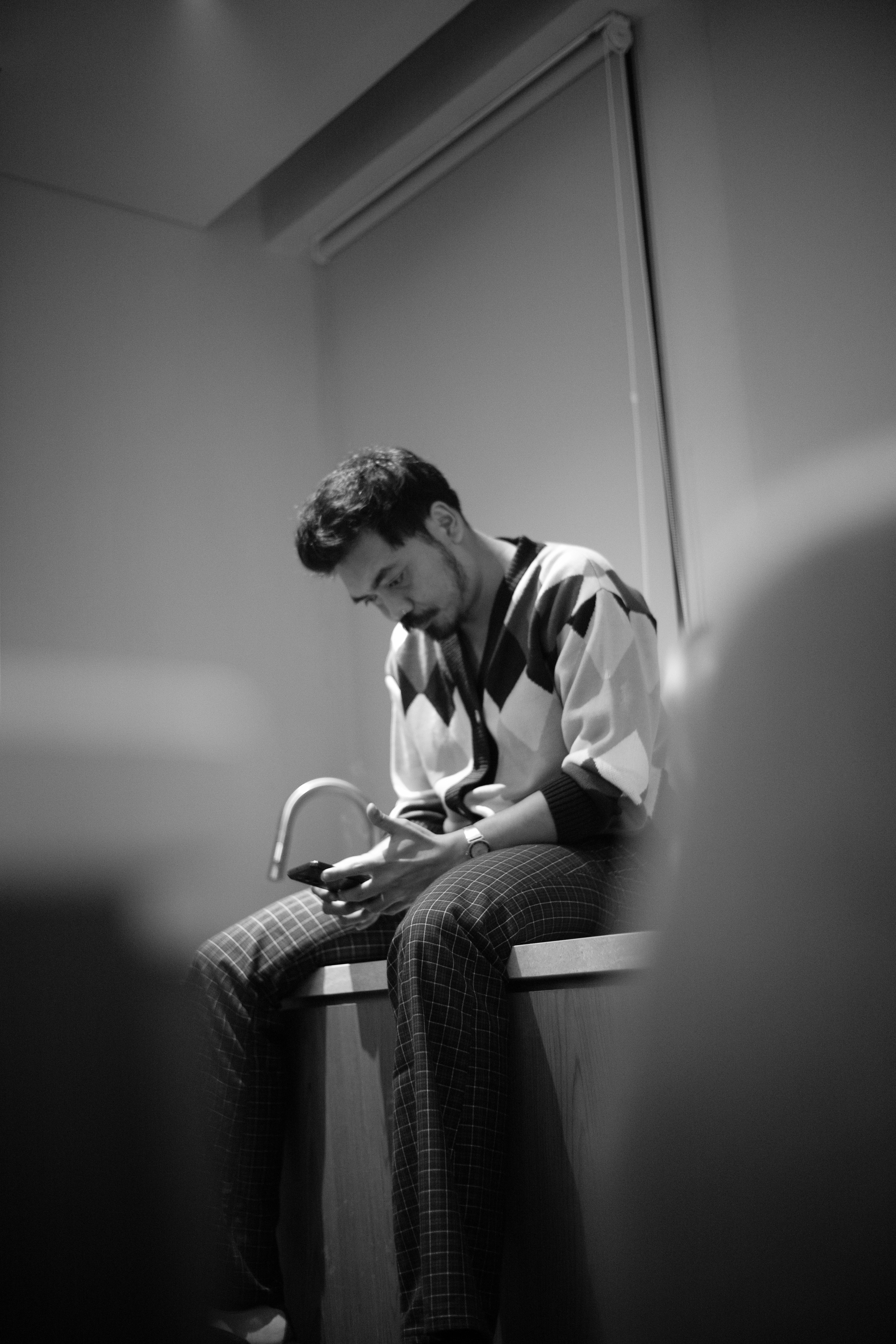 A man in a patterned cardigan and plaid trousers using a smartphone