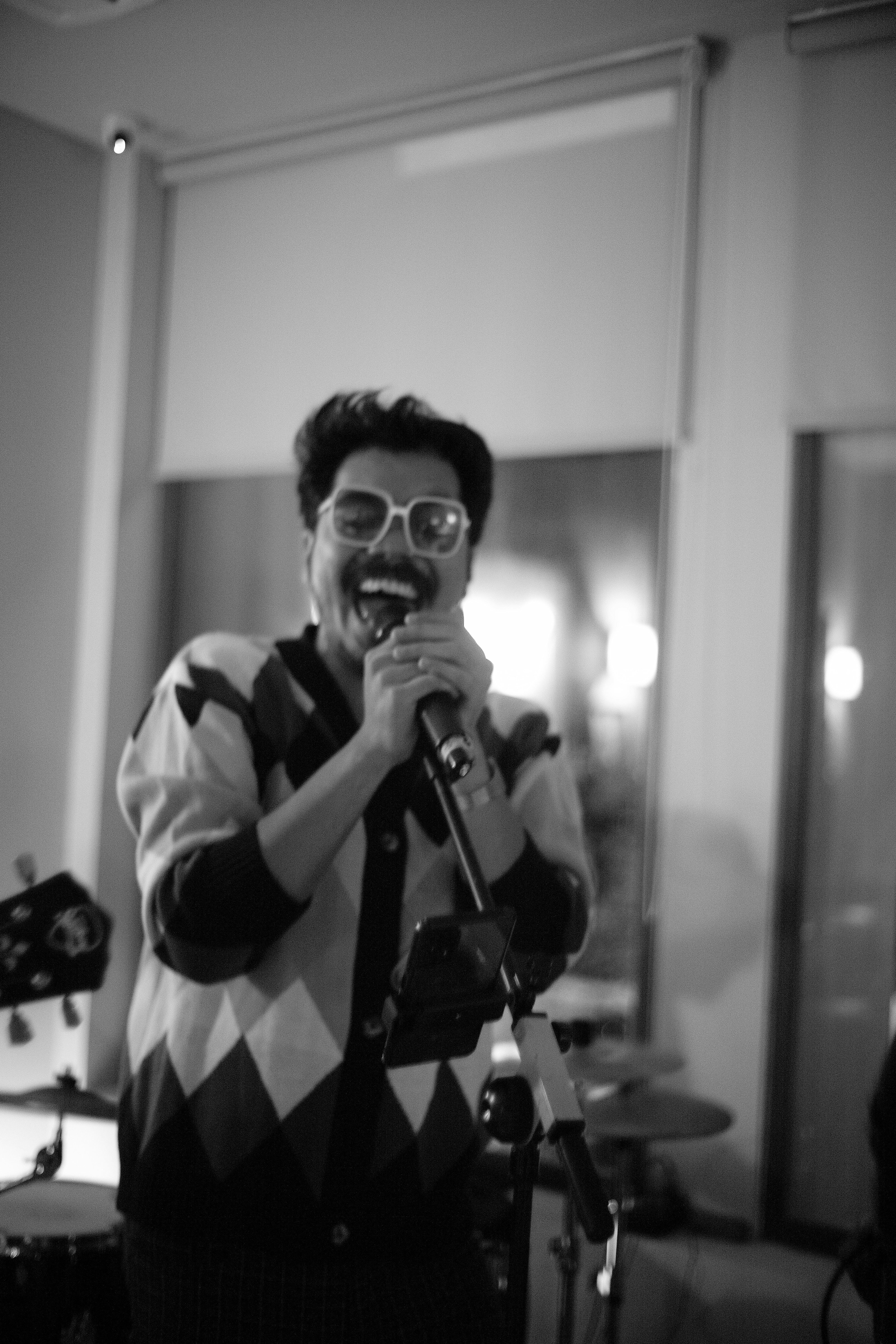 A person with a mustache and glasses singing into a microphone on stage
