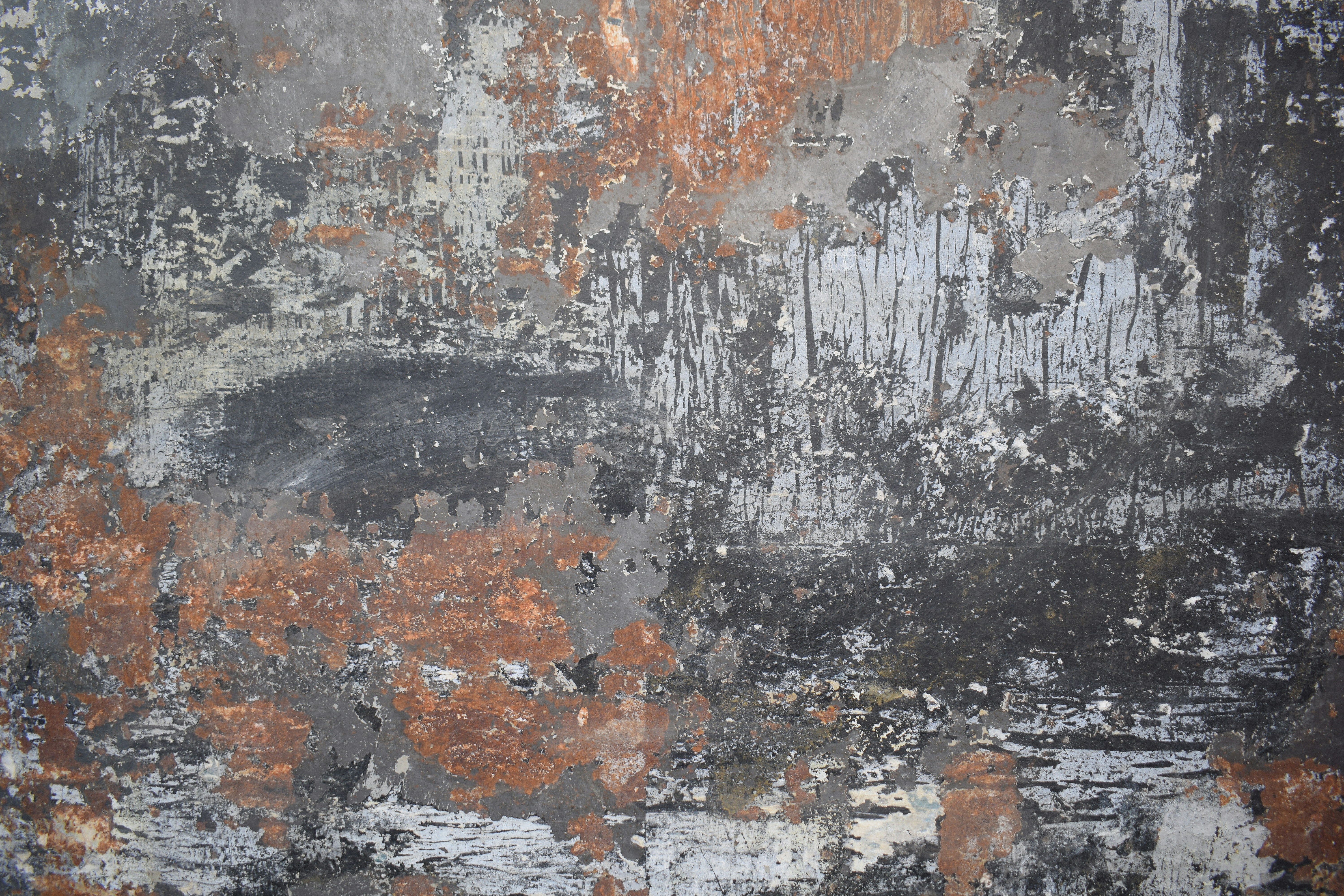 A weathered wall surface with peeling grey paint and patches of rusted metal