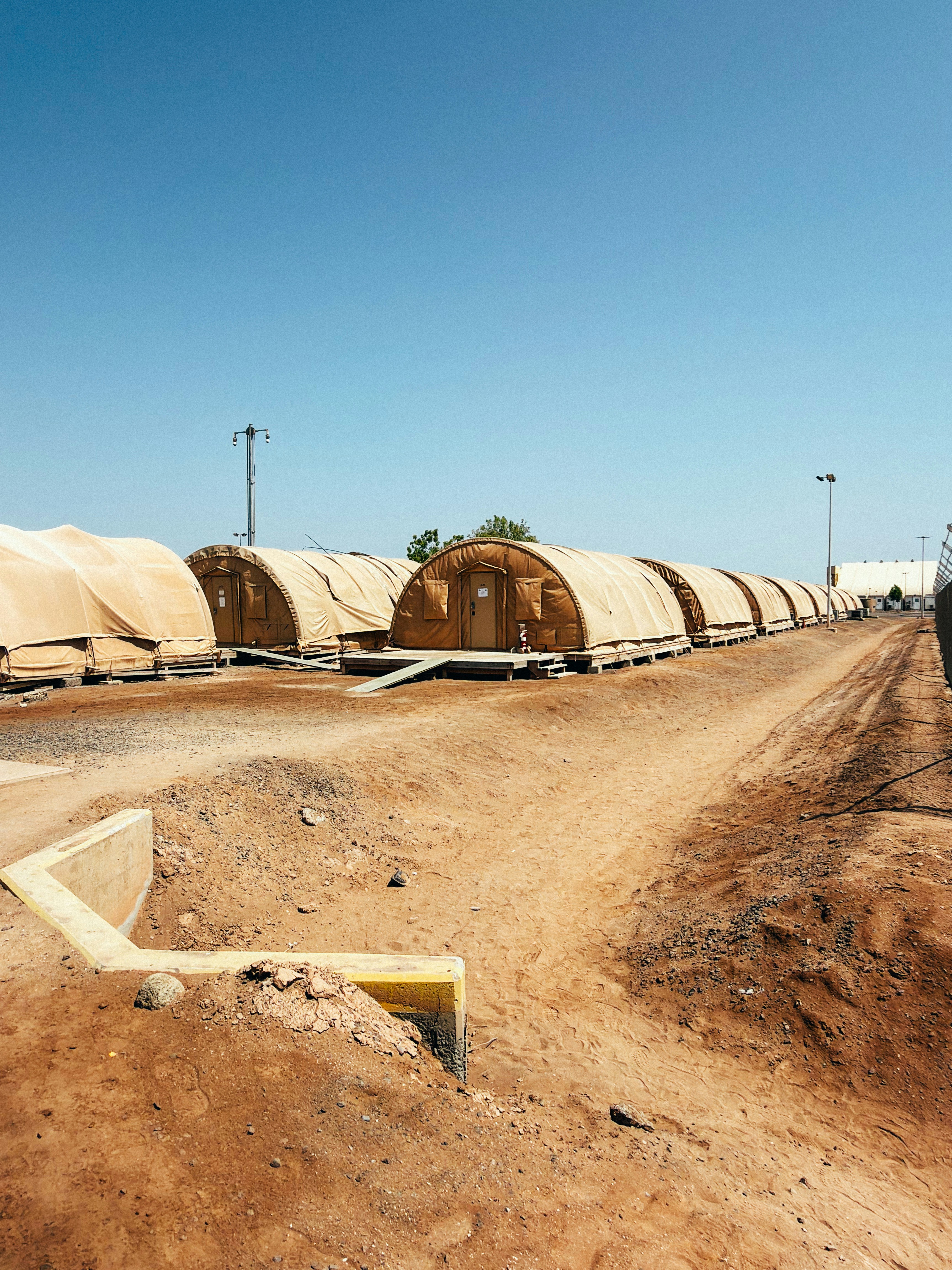 A row of tan arched tents on wooden platforms in a dusty desert camp