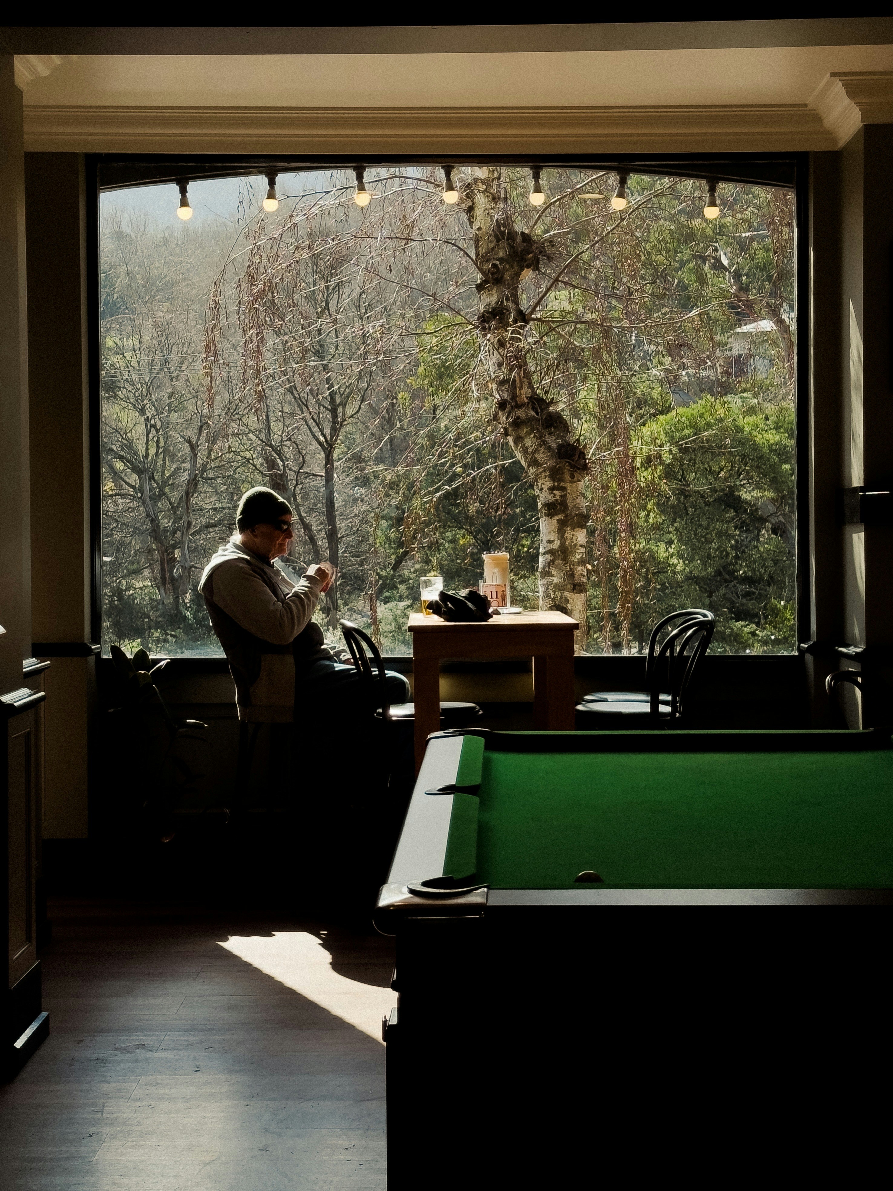A person in a beanie sitting at a table by a large window