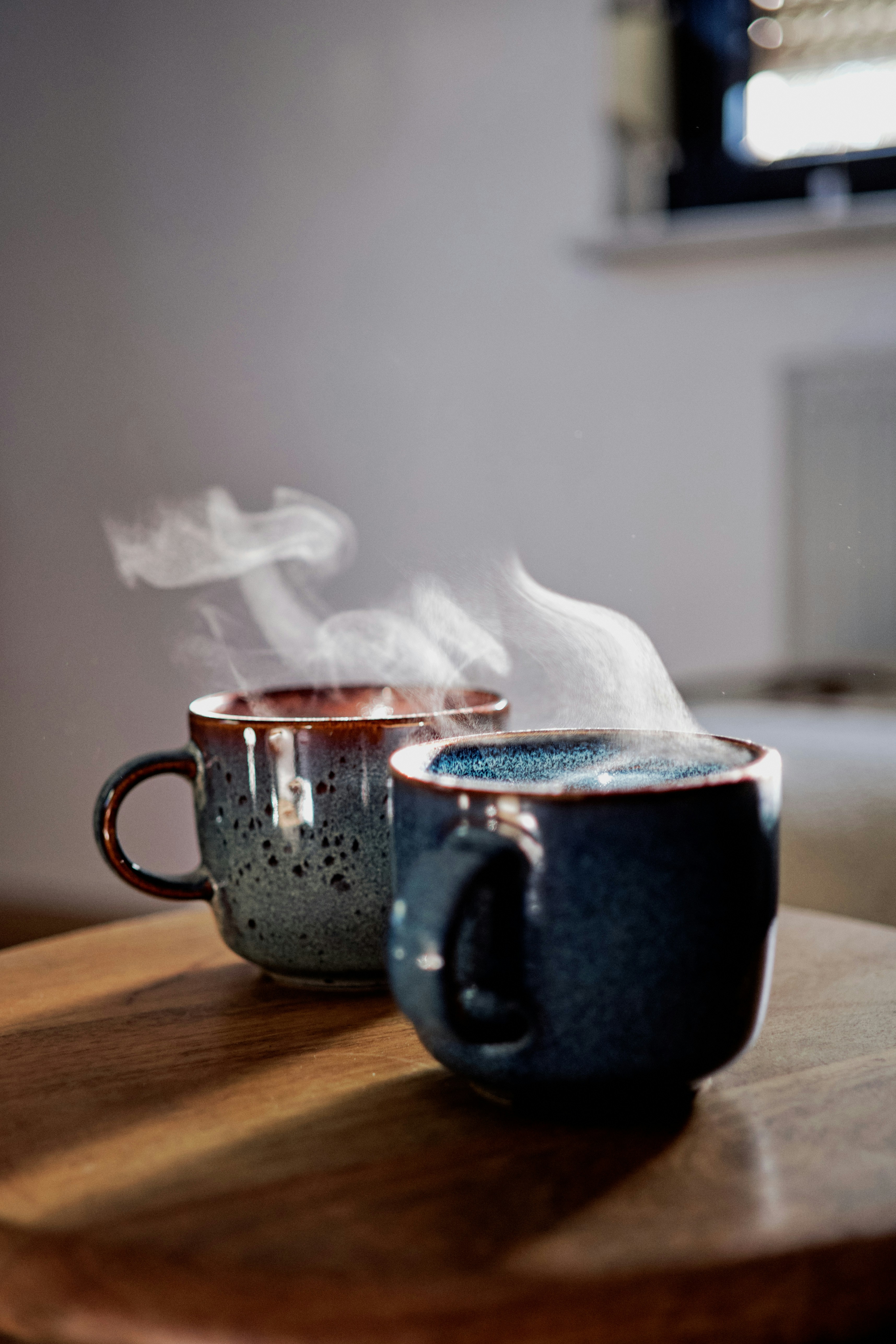Two steaming ceramic mugs on a wooden table in a sunlit room