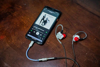 A smartphone playing music with wired in-ear monitors connected via a dongle adapter