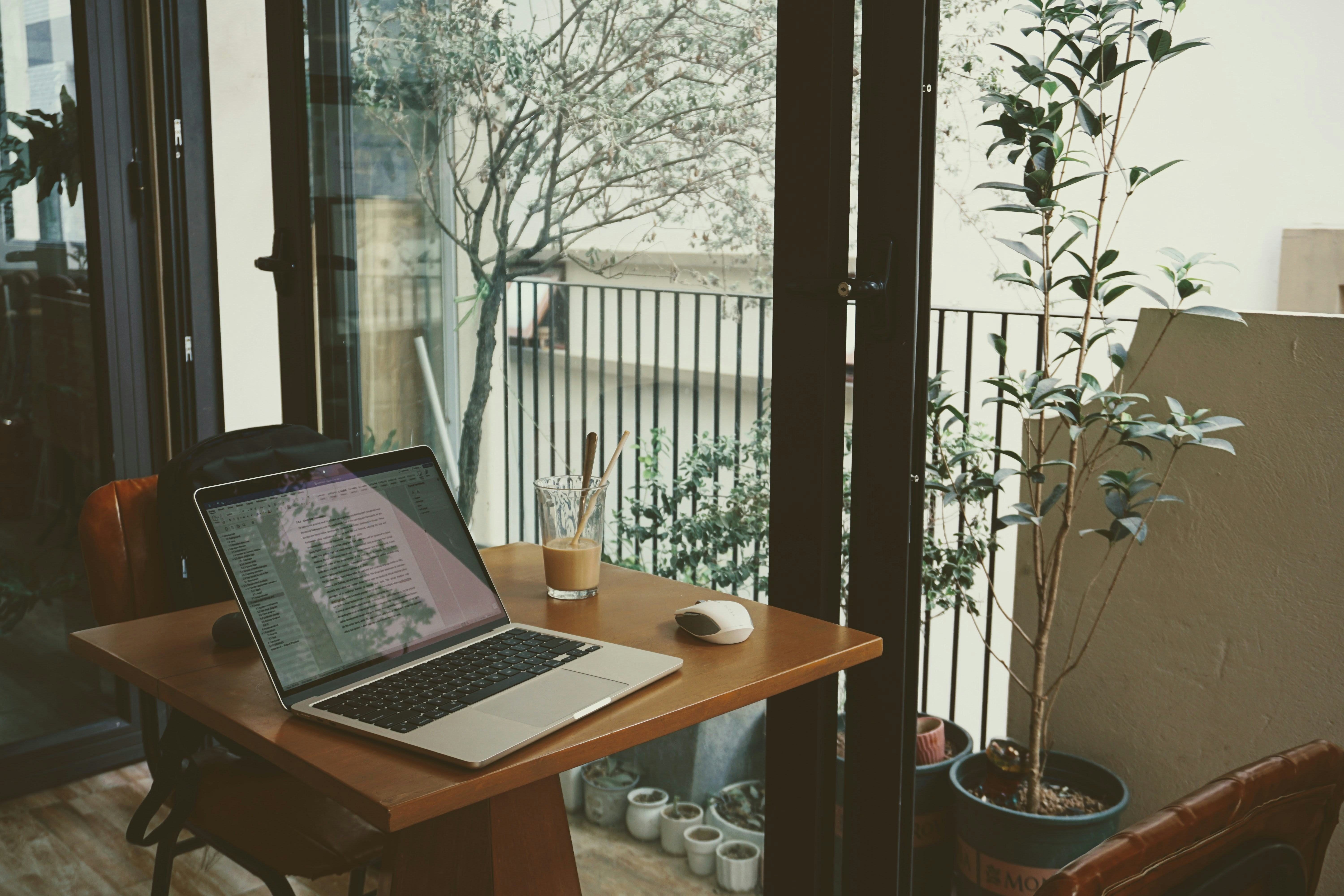 Um laptop em uma mesa de madeira com um copo de café gelado