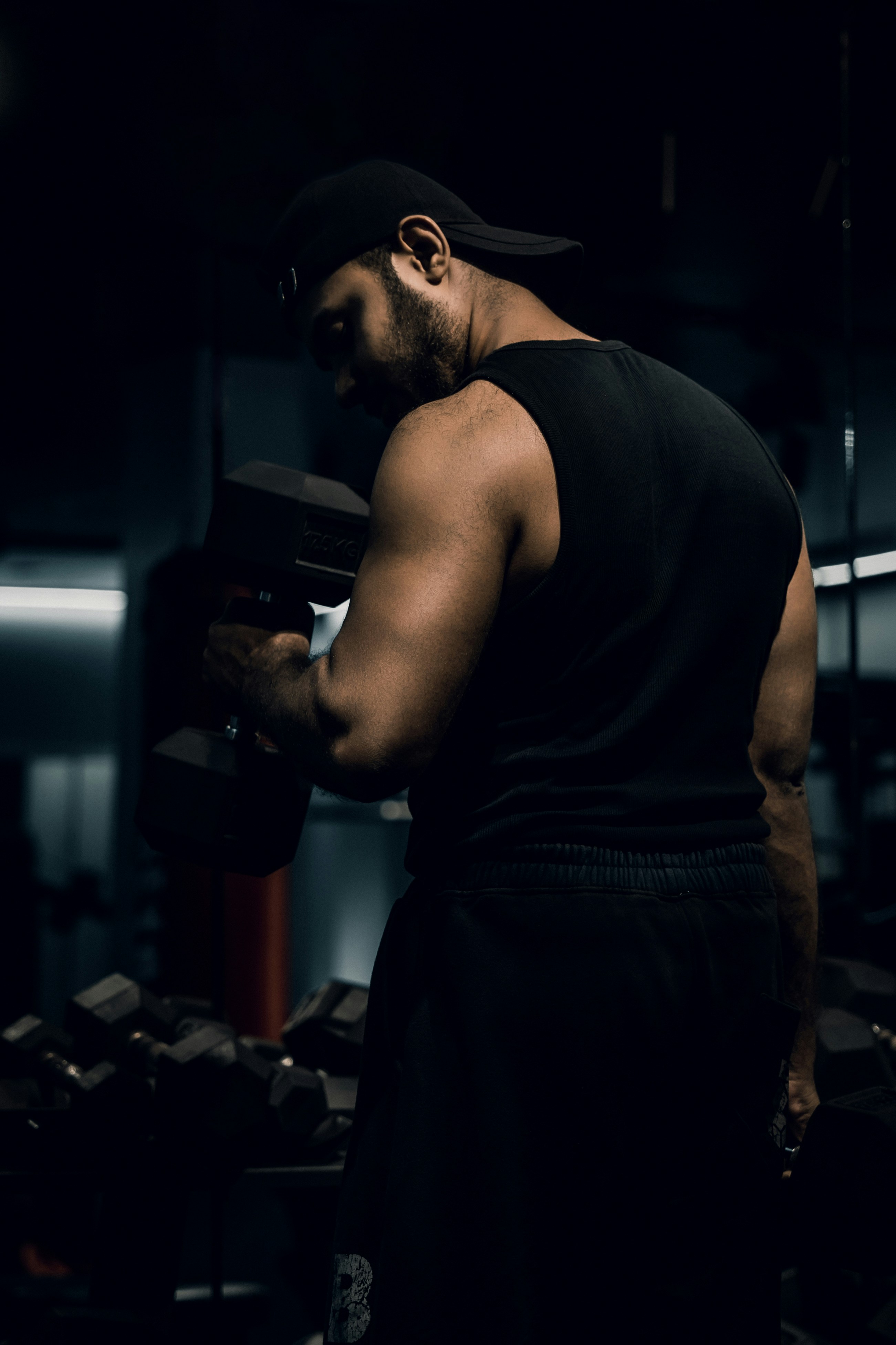 A man in a black tank top lifting a dumbbell in a gym