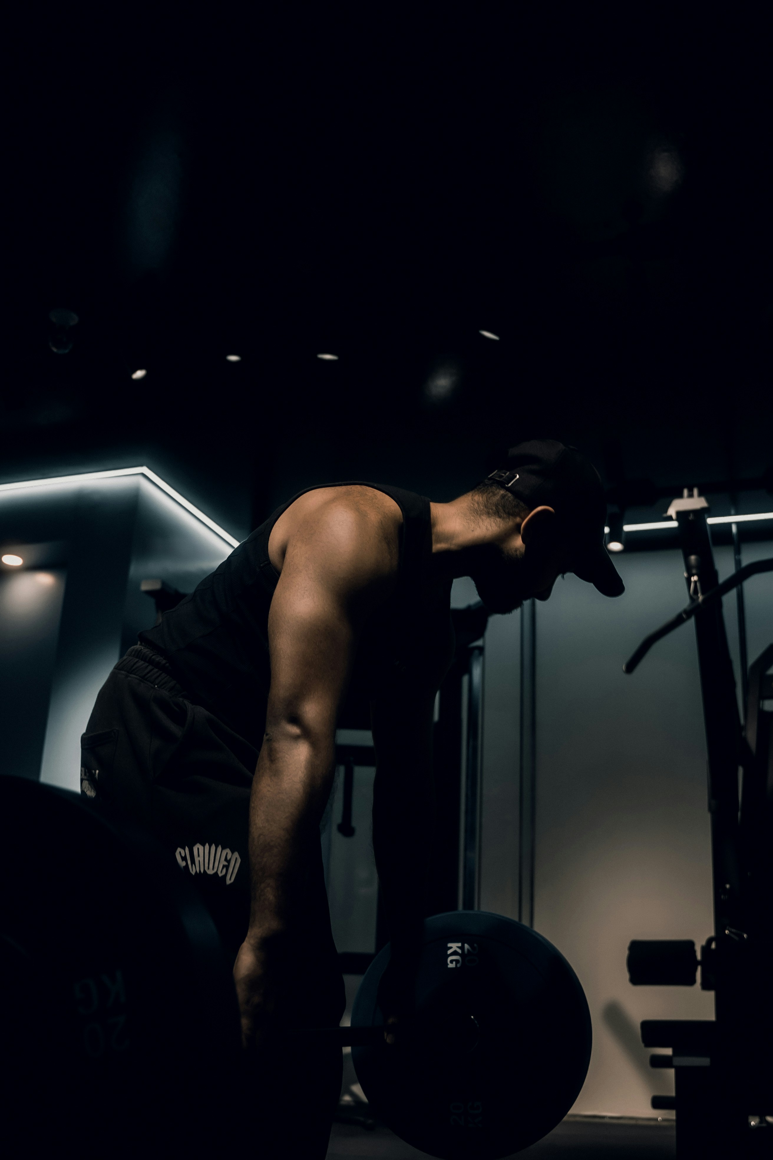 A person in a black tank top and cap lifting a barbell in a gym