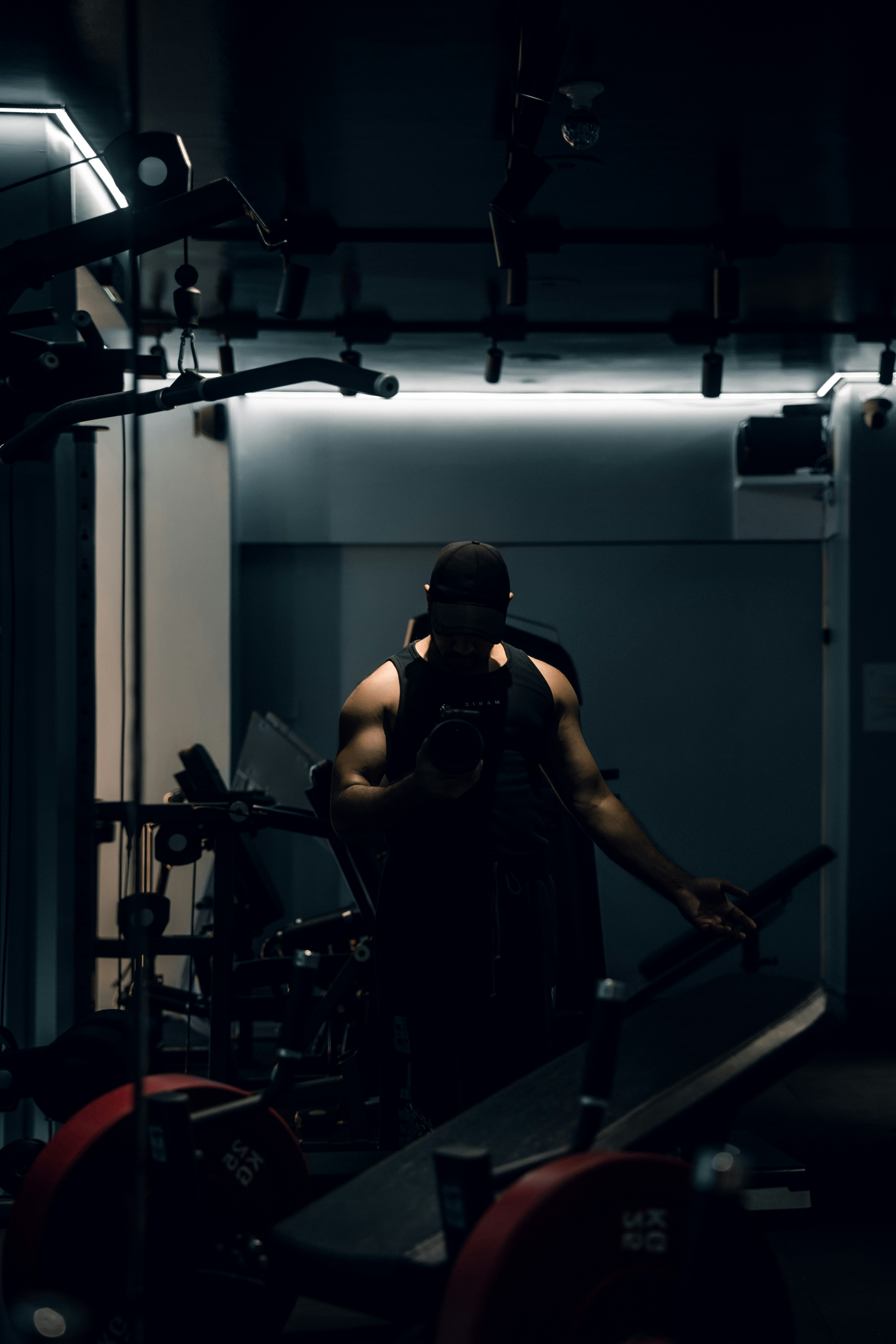A person in a black tank top and cap holding a camera in a gym