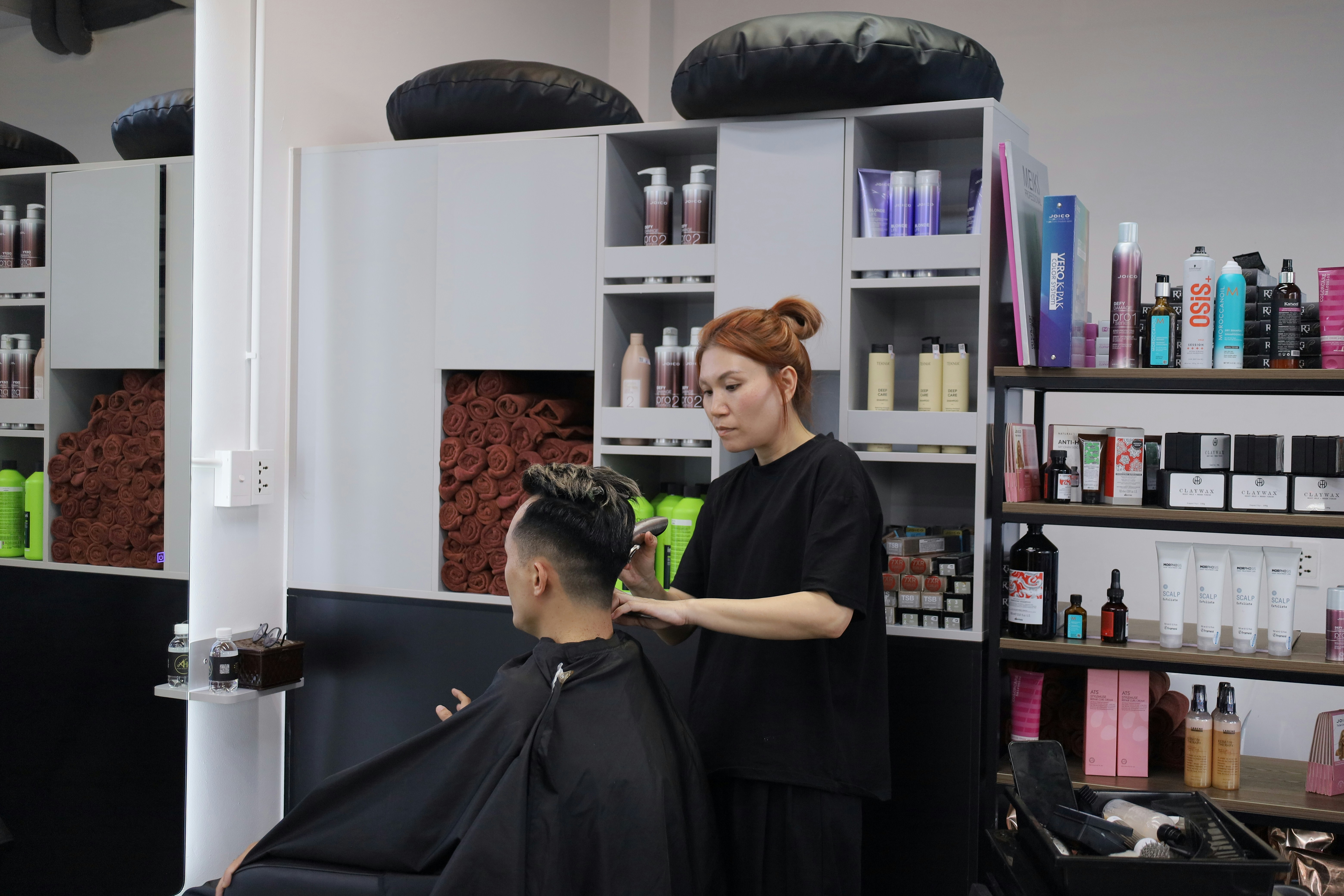 A woman cutting a man's hair with clippers in a hair salon