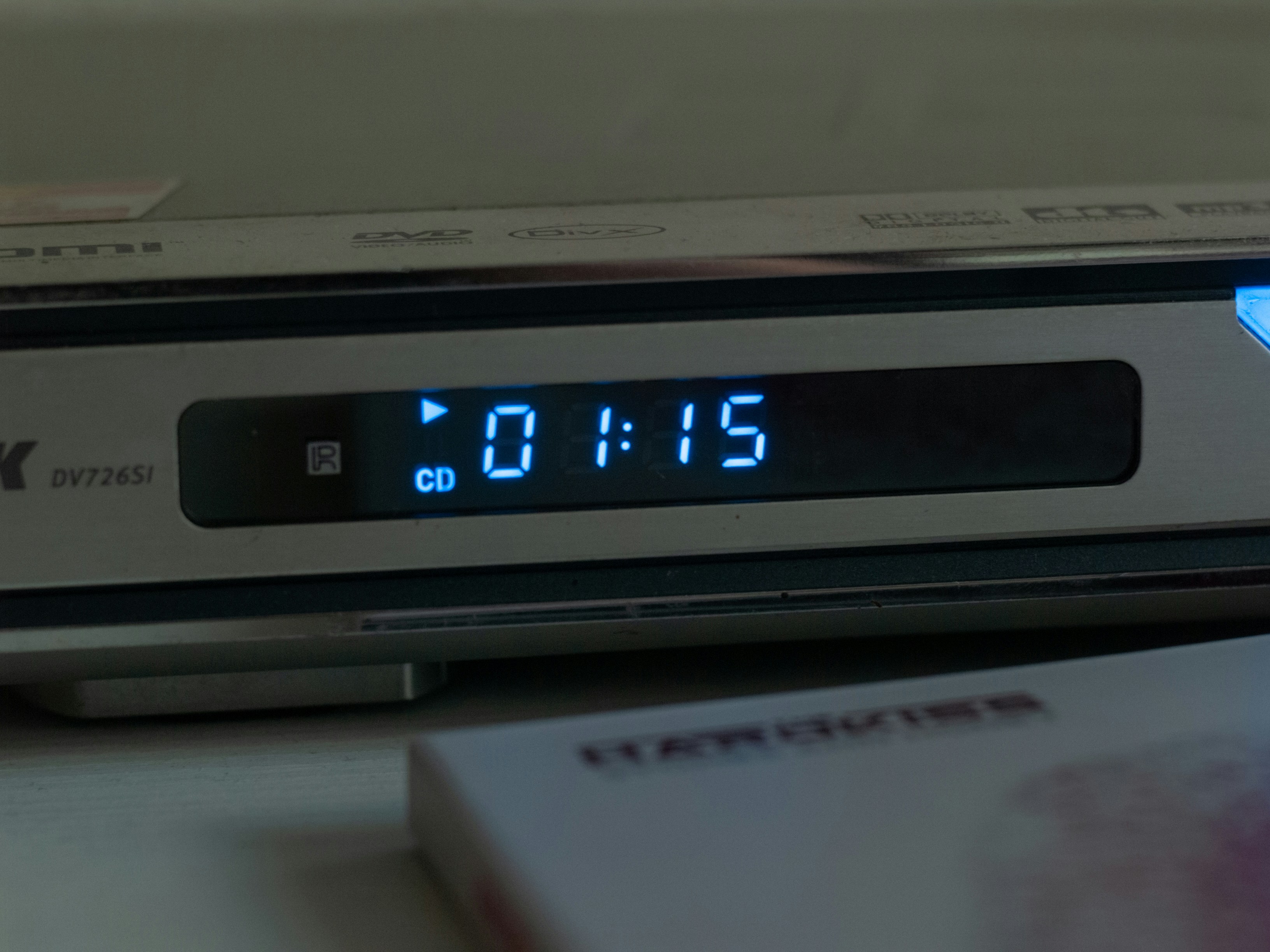 A silver DVD player with a glowing blue digital display showing 01:15