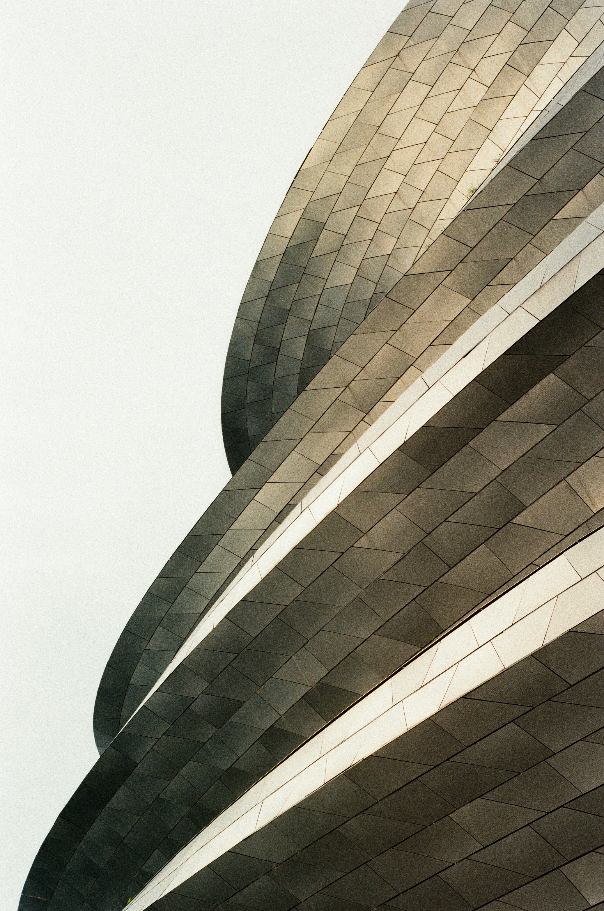 Curved architectural facade with overlapping dark grey metal panels and light horizontal lines