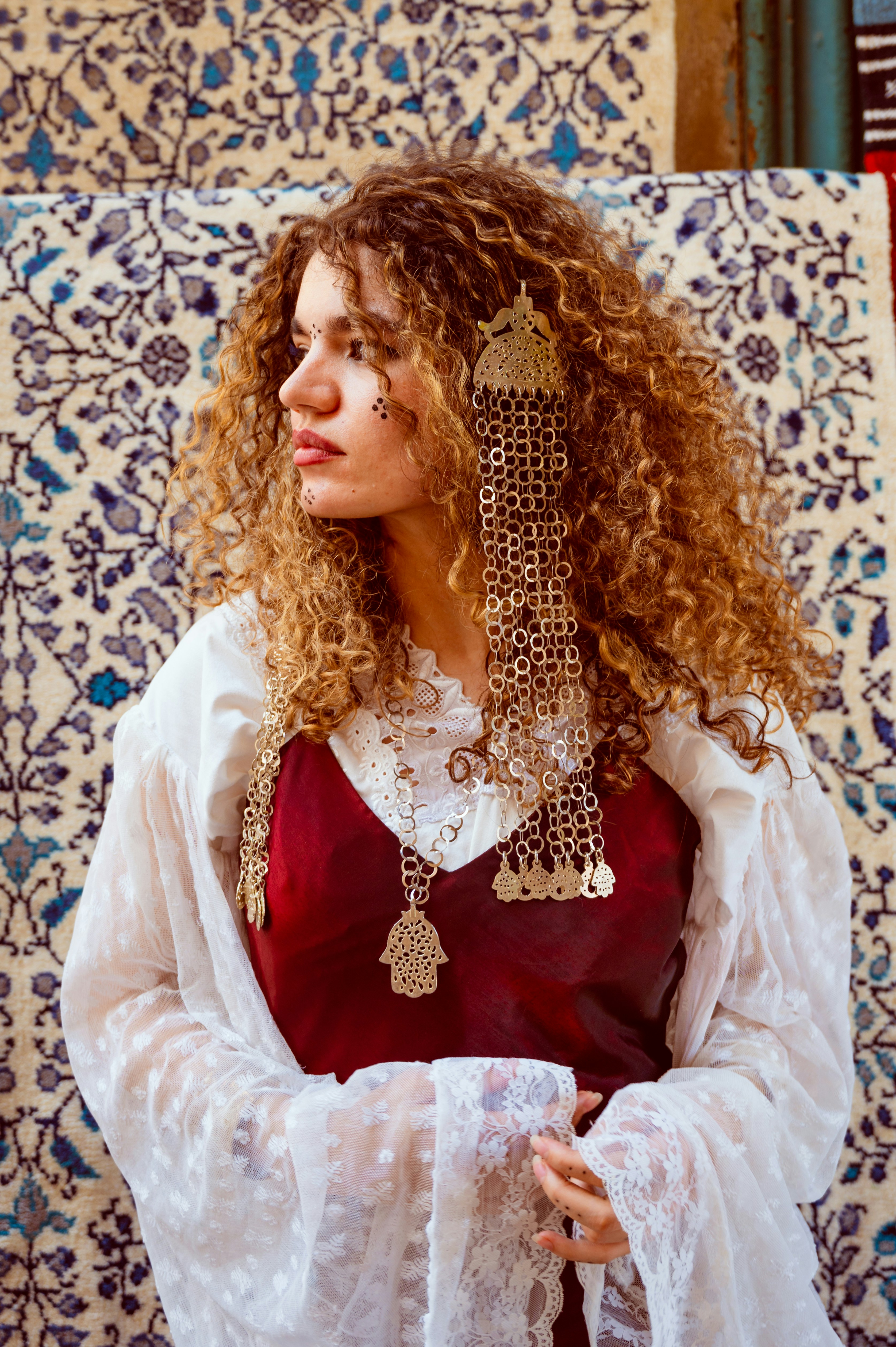 A woman with curly hair wearing a red dress and ornate metal jewelry