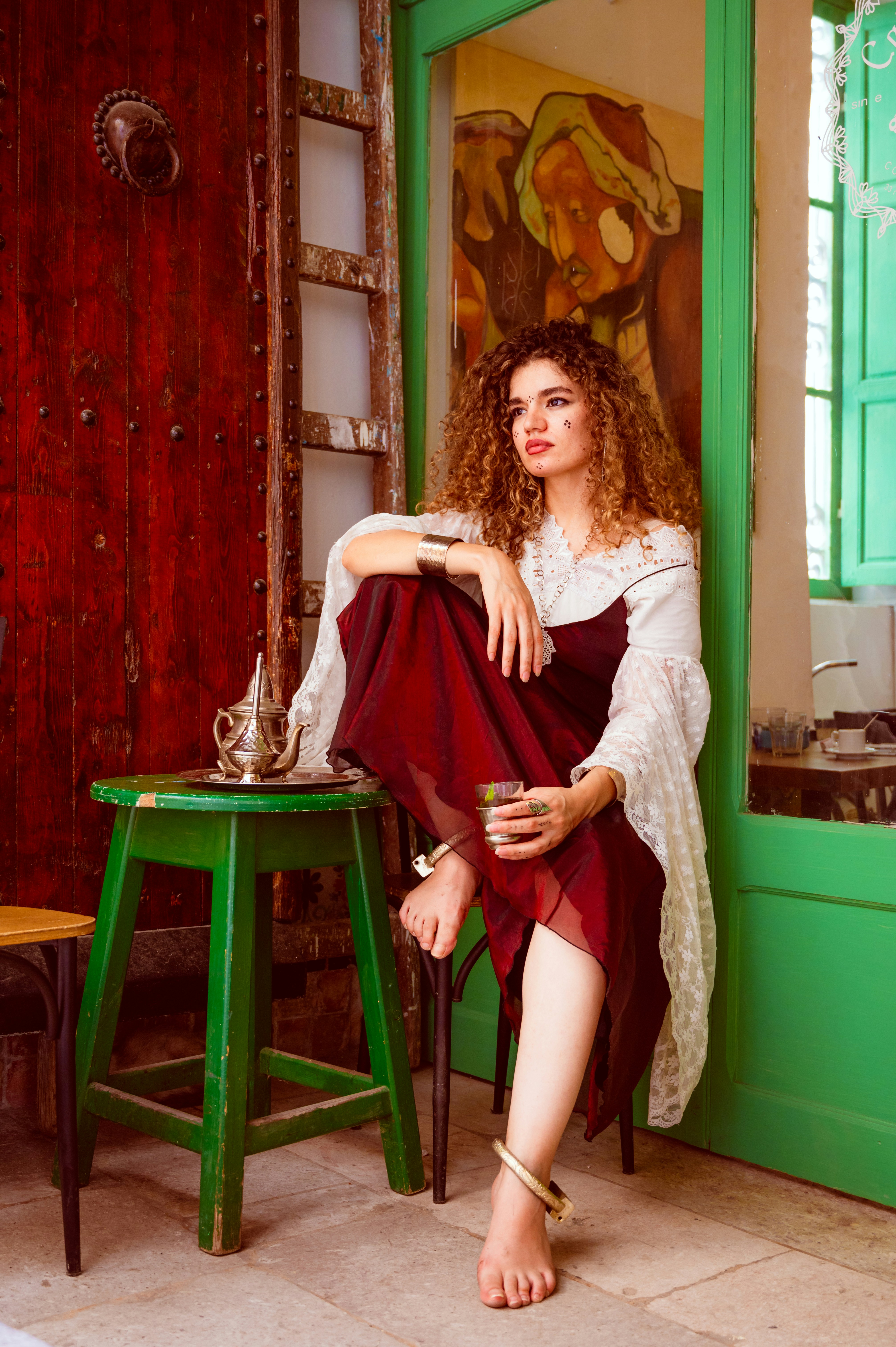 A woman with curly hair in a maroon dress holding a glass of tea