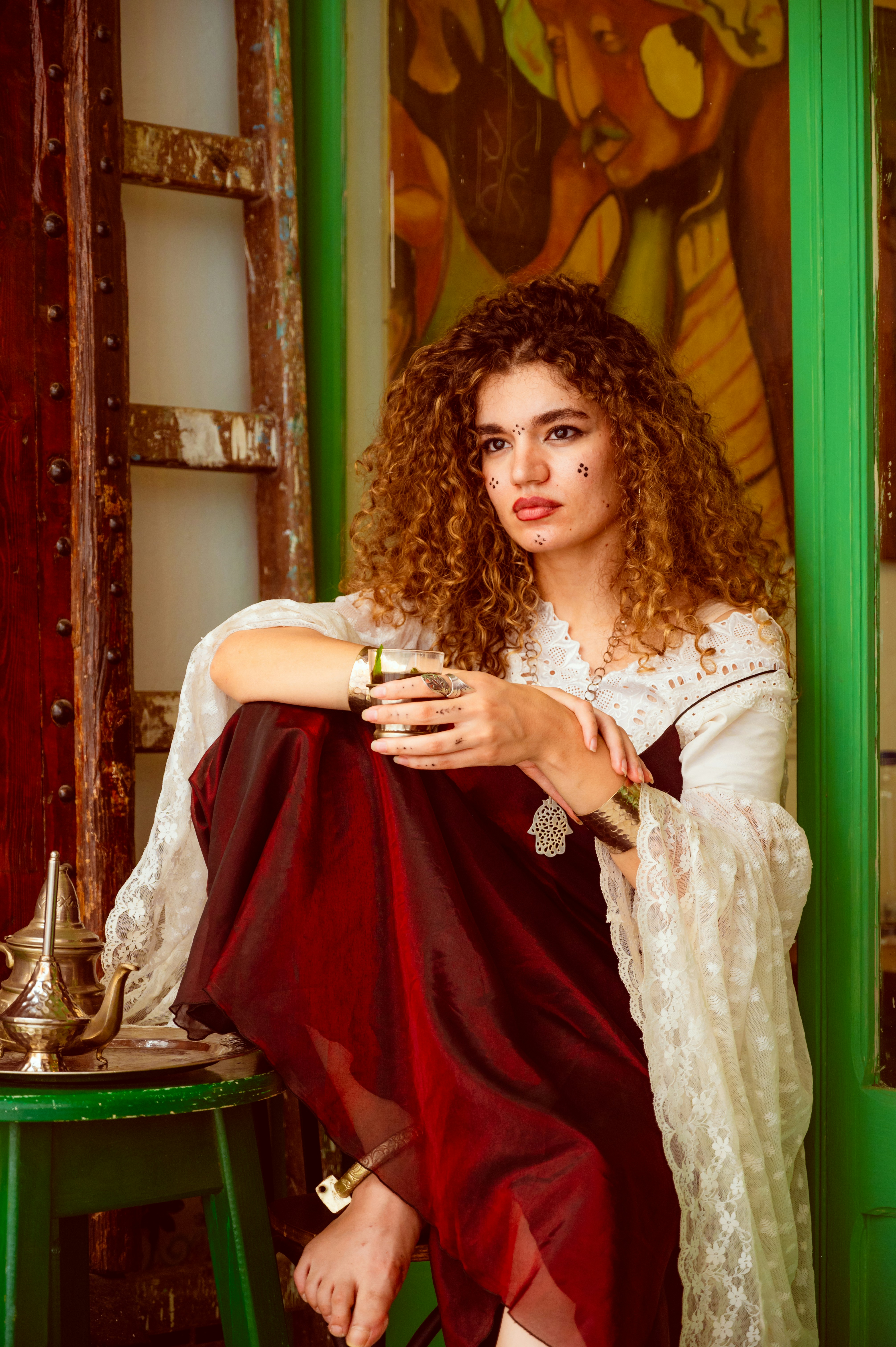 A woman with curly hair in a dark dress and lace sleeves holding a glass