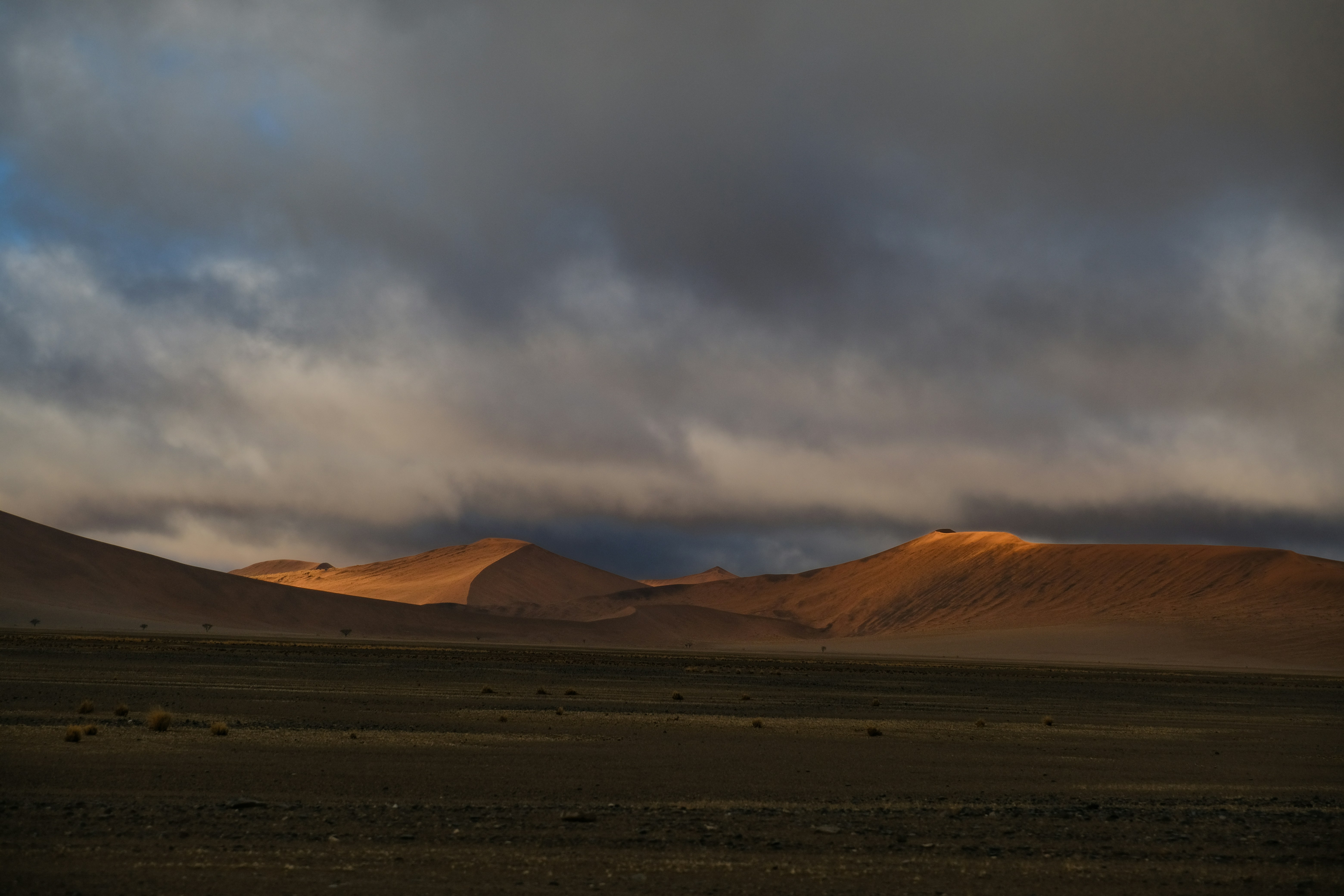 Golden light on sand dunes beneath a heavy layer of dark storm clouds