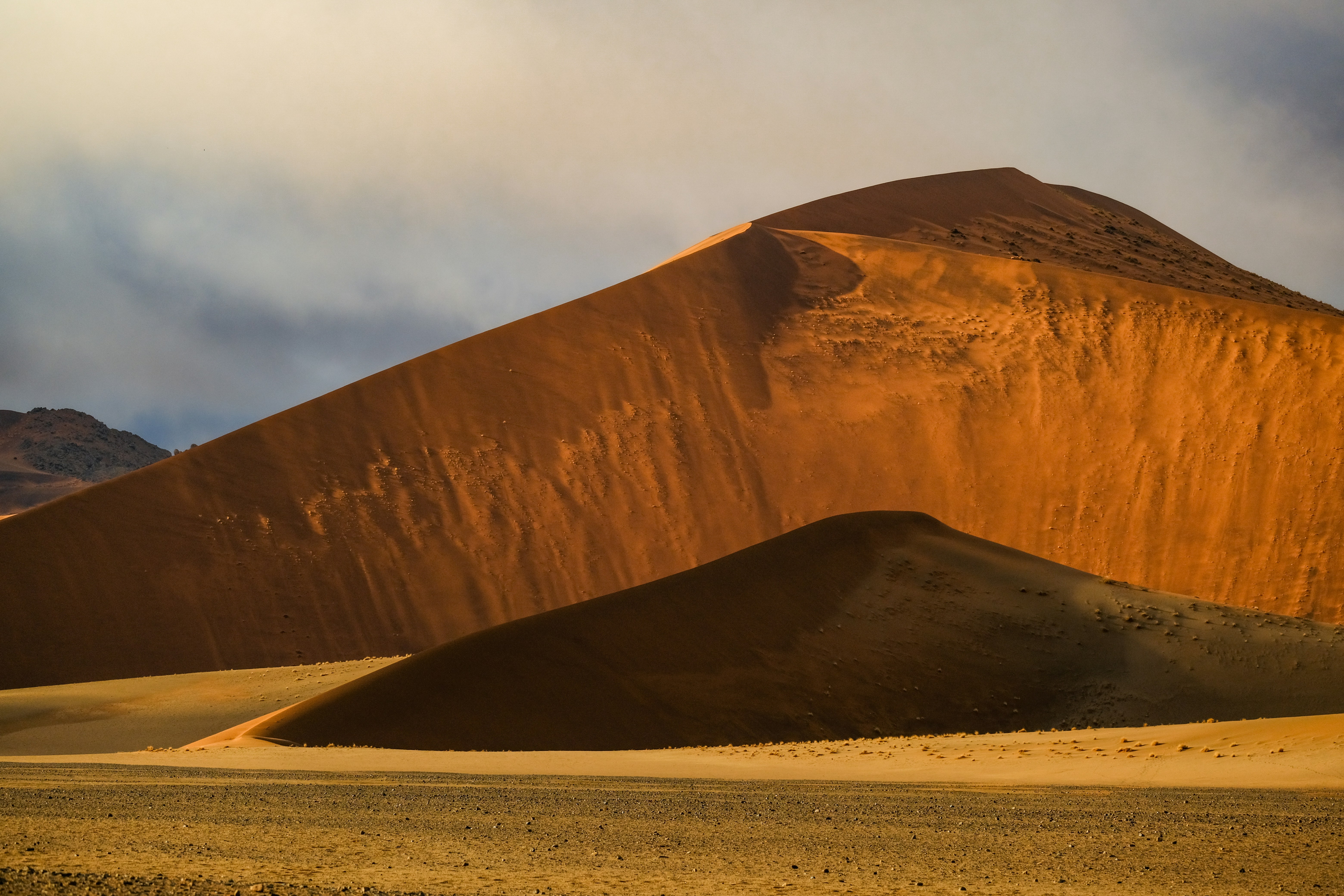 Large orange sand dunes under a cloudy sky in the Namib Desert
