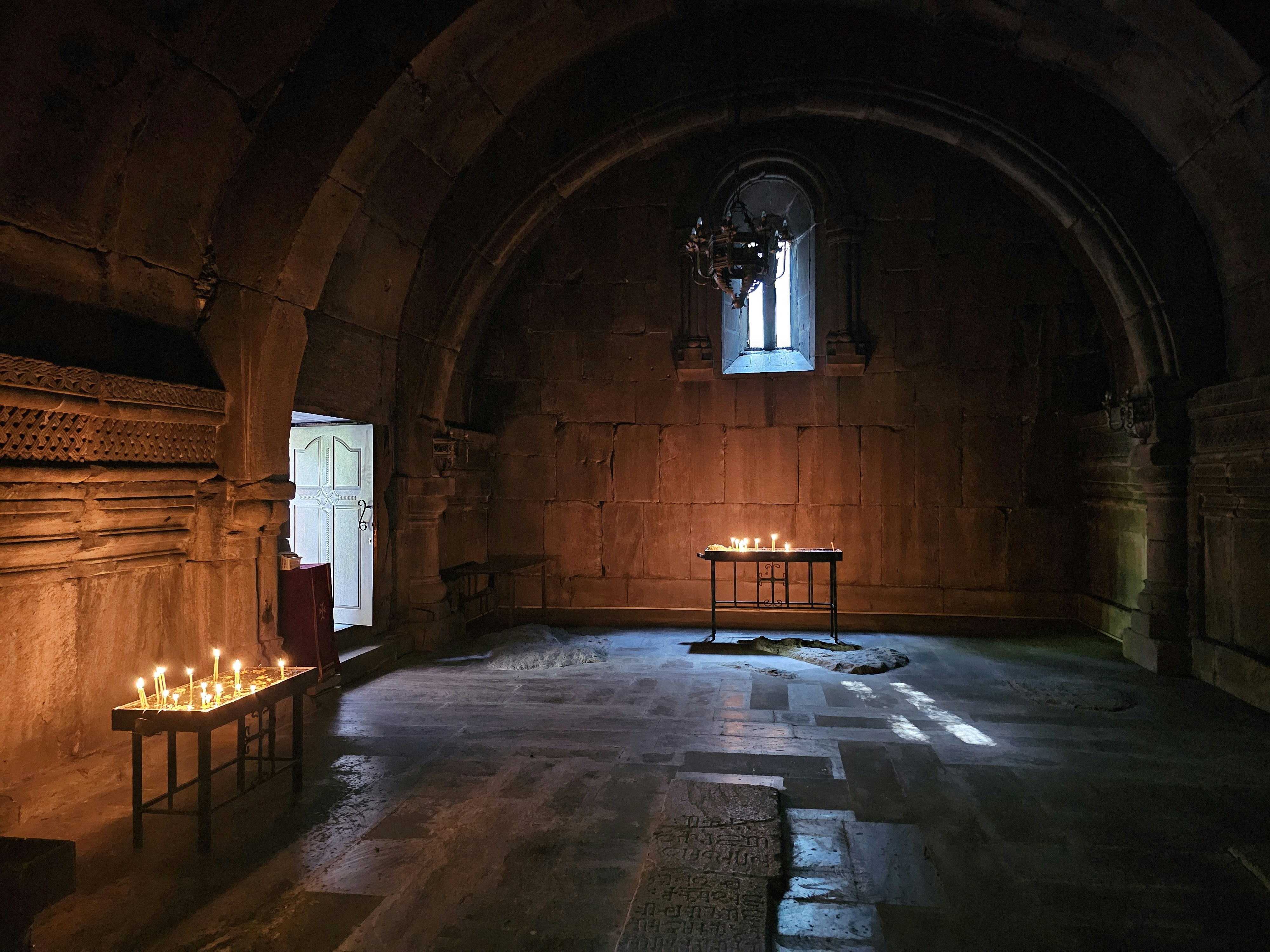 Candles burning on metal stands inside a dim stone church with arched walls