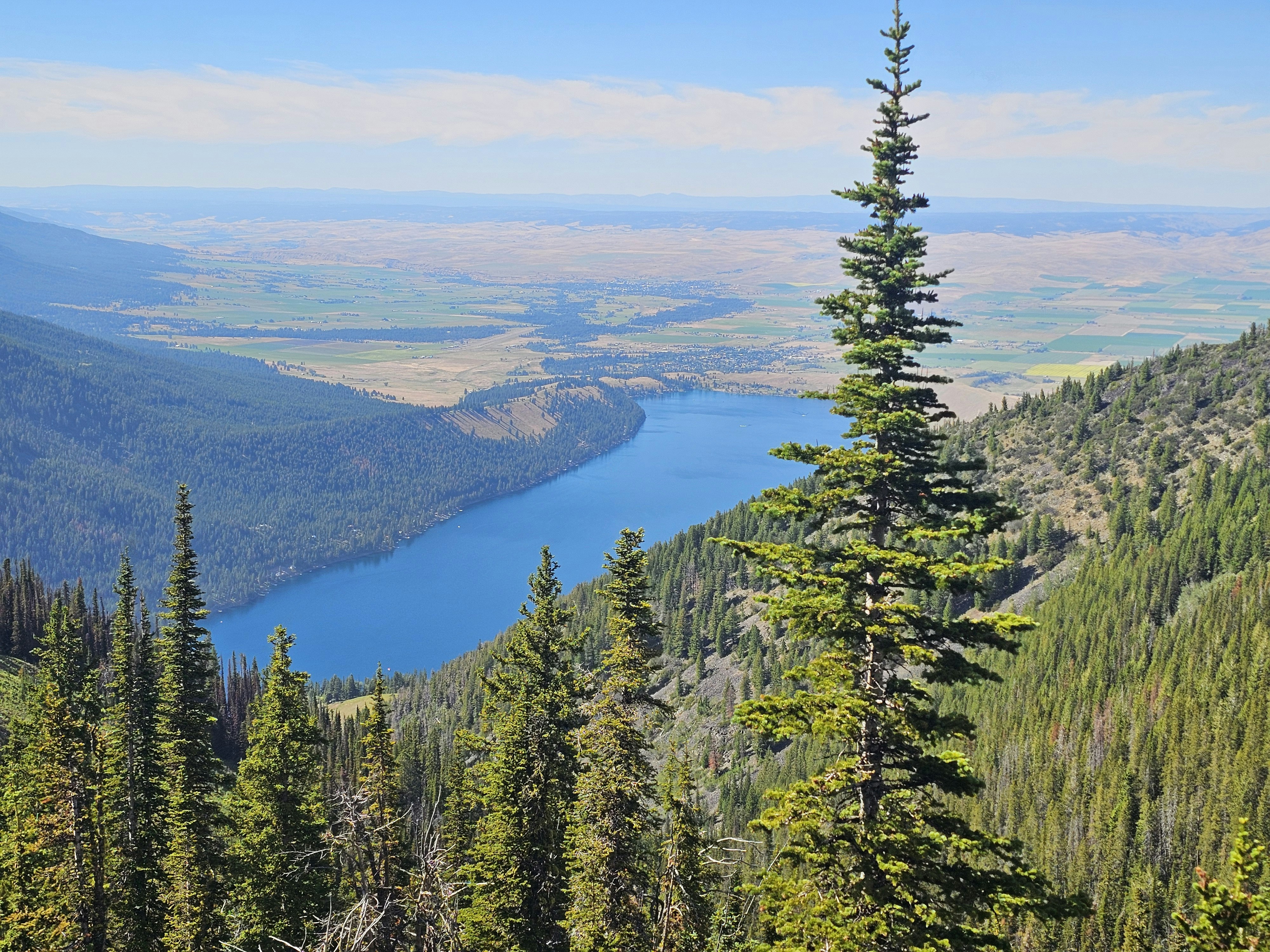 A deep blue lake nestled between forested mountain slopes and a distant valley