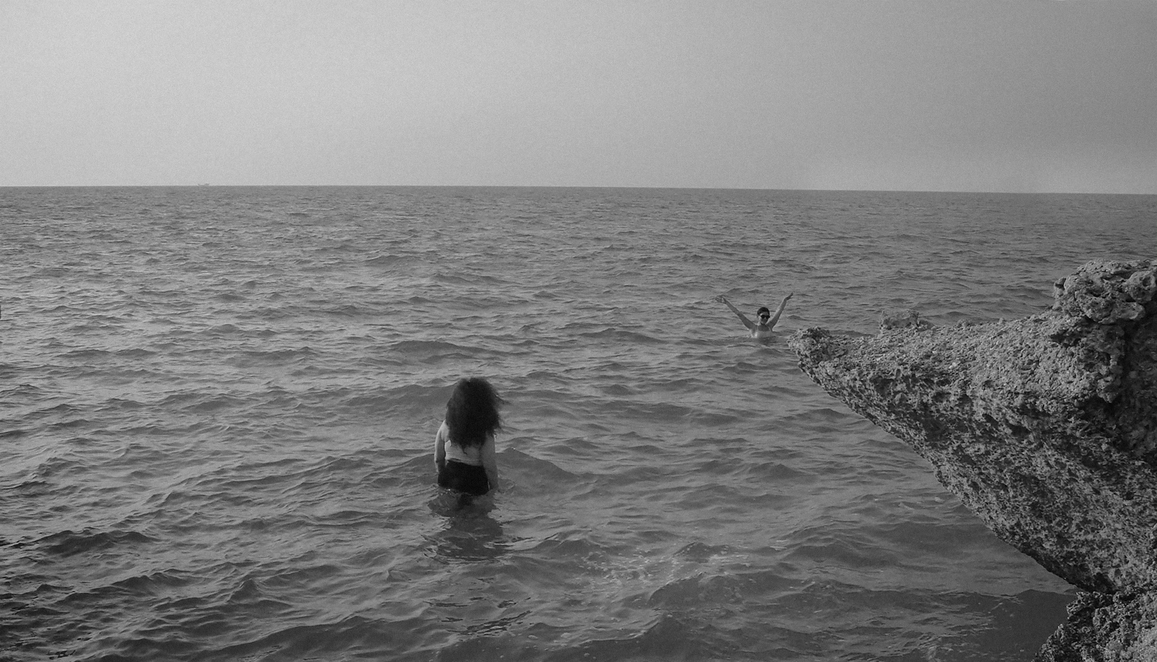 Two people in the sea near a rocky shore in Kish, Iran