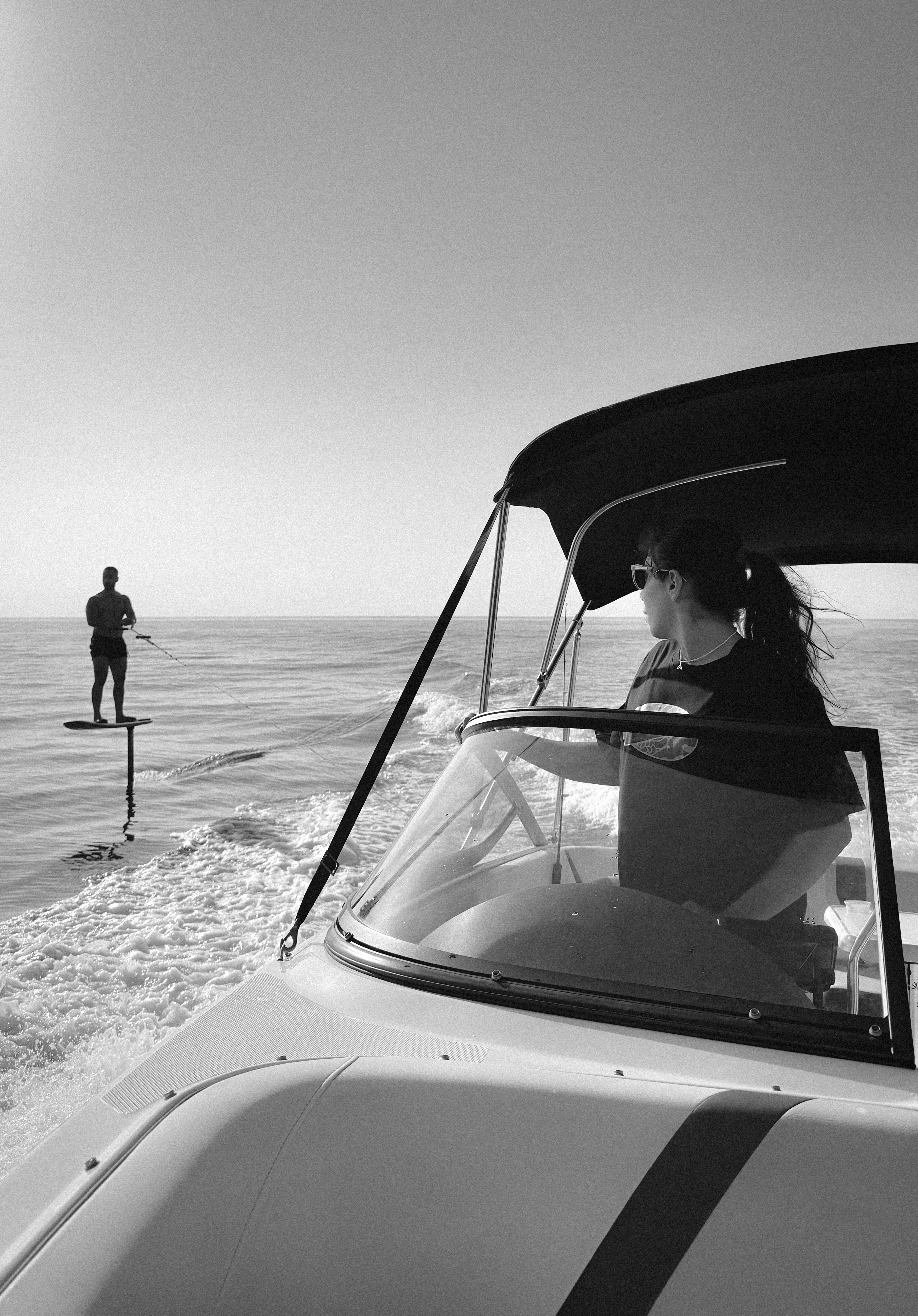 A person driving a motorboat while another person rides a hydrofoil board nearby