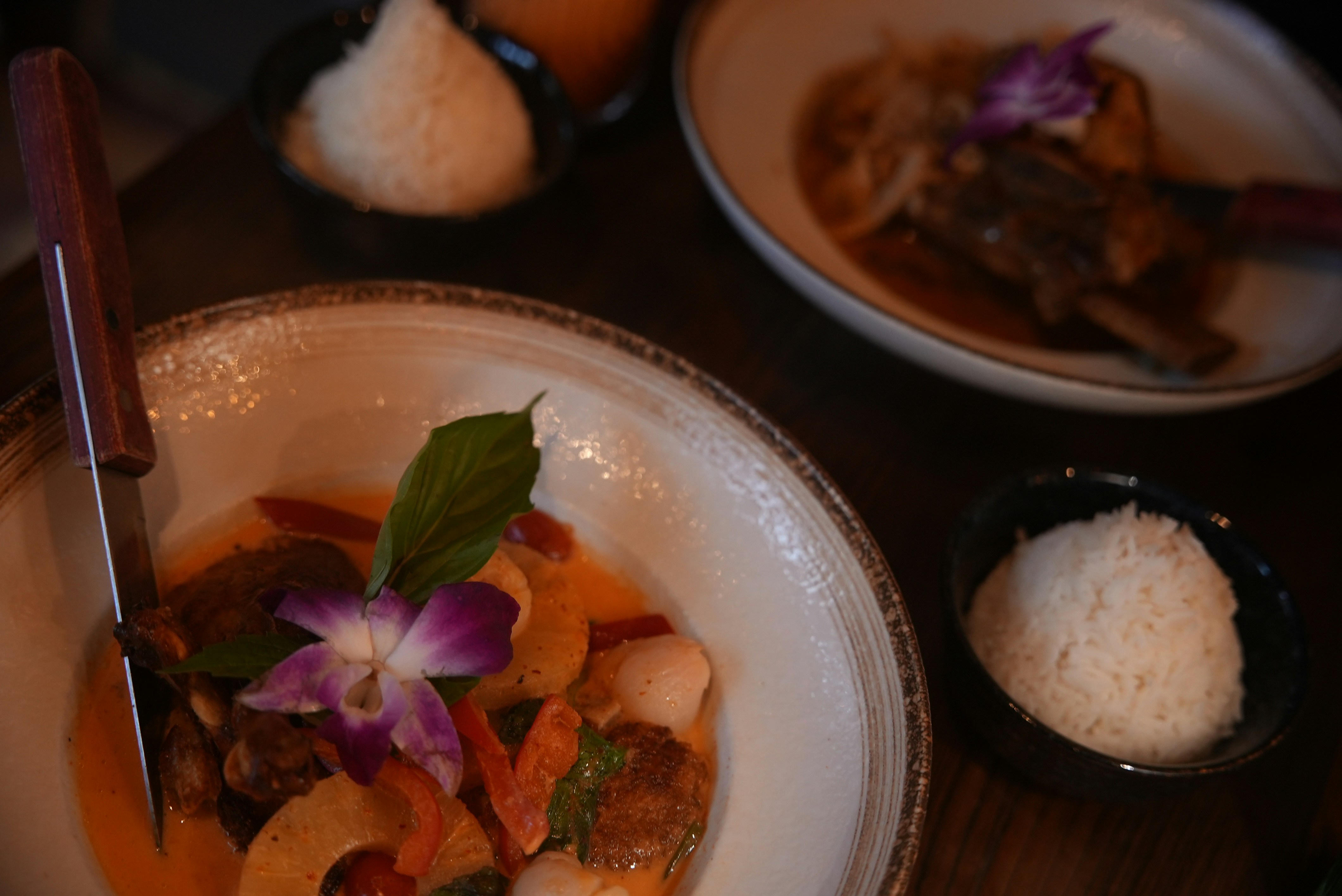 A bowl of red curry with pineapple and a purple orchid garnish