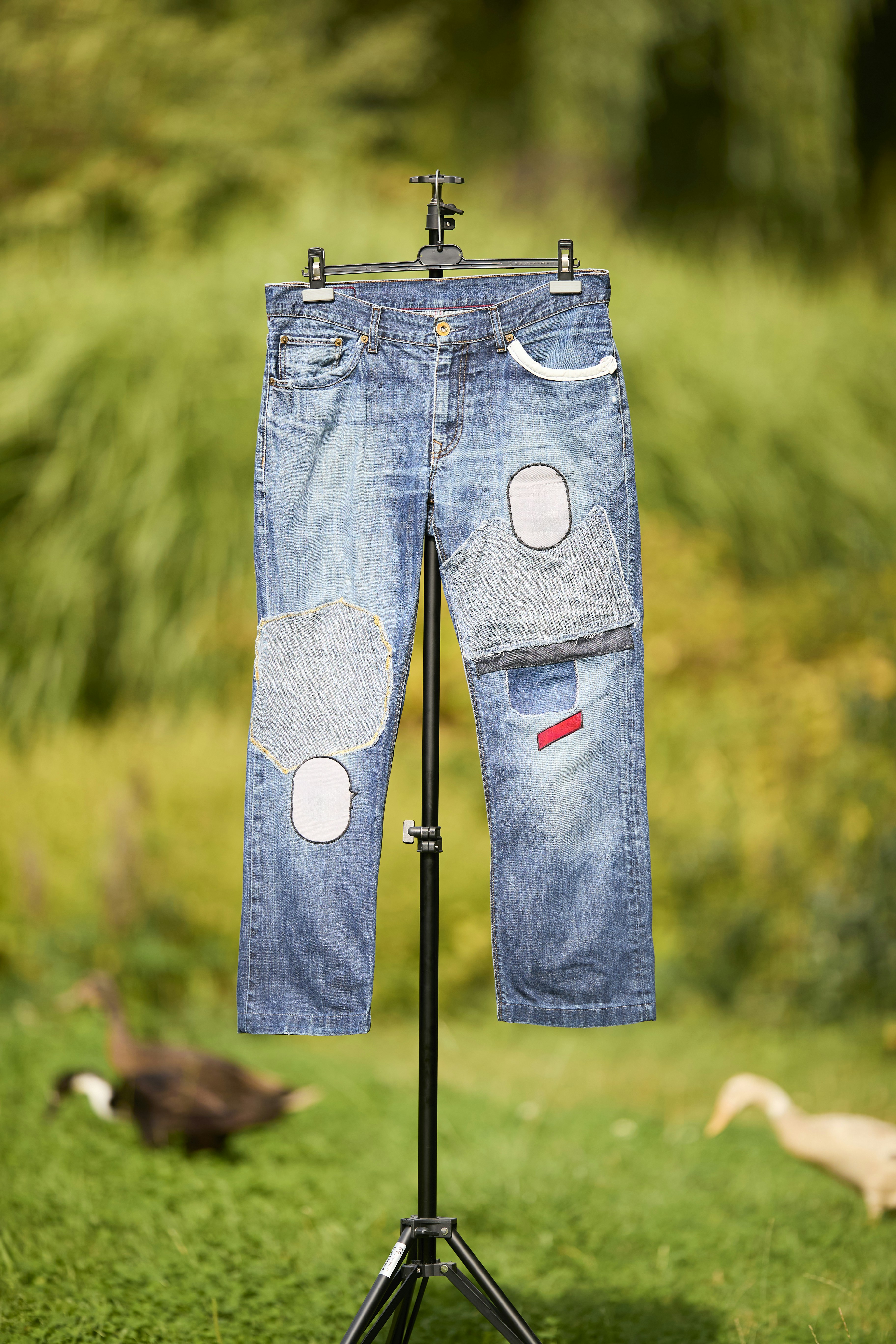 Blue denim jeans with various patches hanging on a tripod in a garden