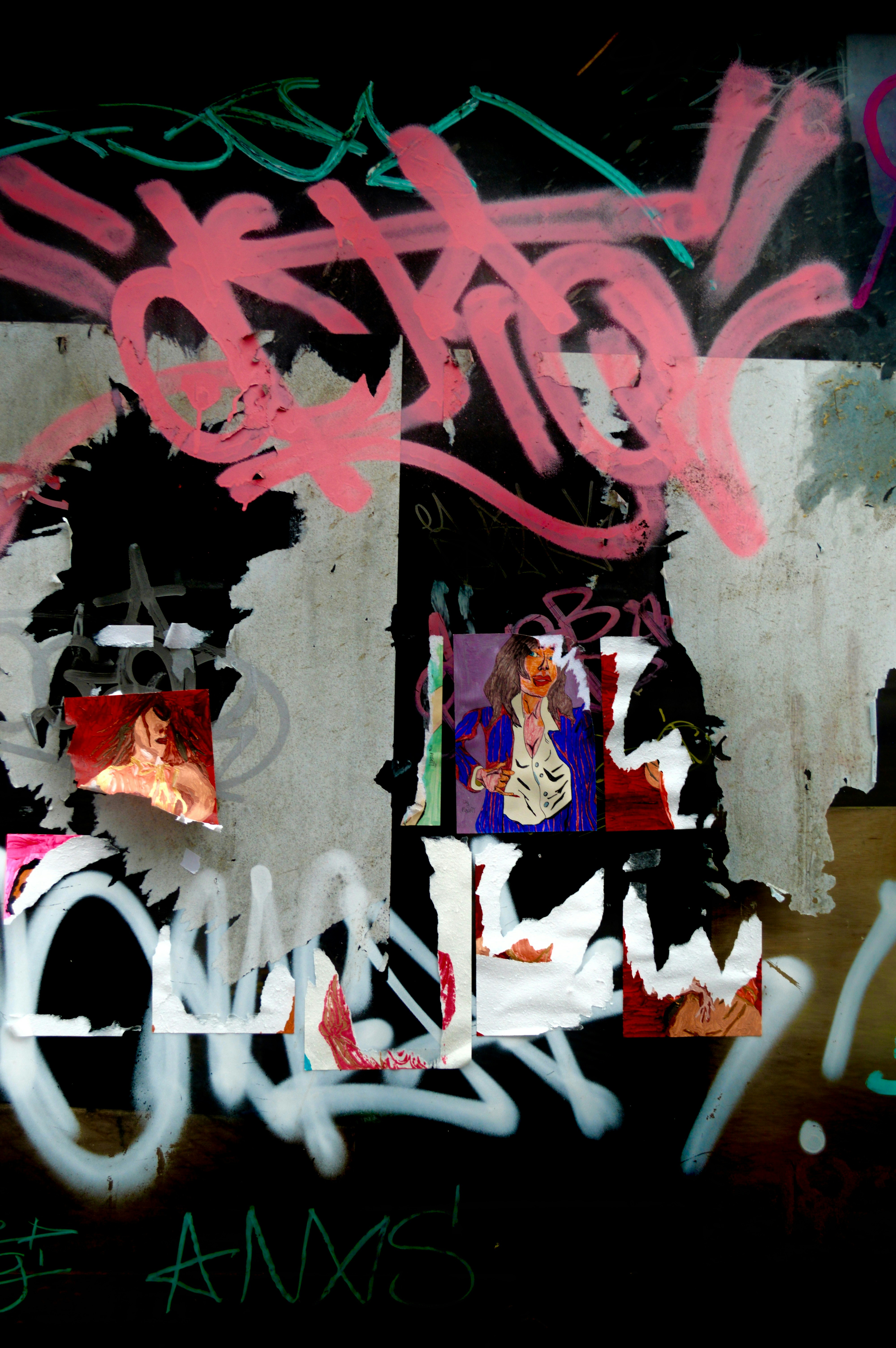 Torn posters and pink graffiti on a dark weathered wall