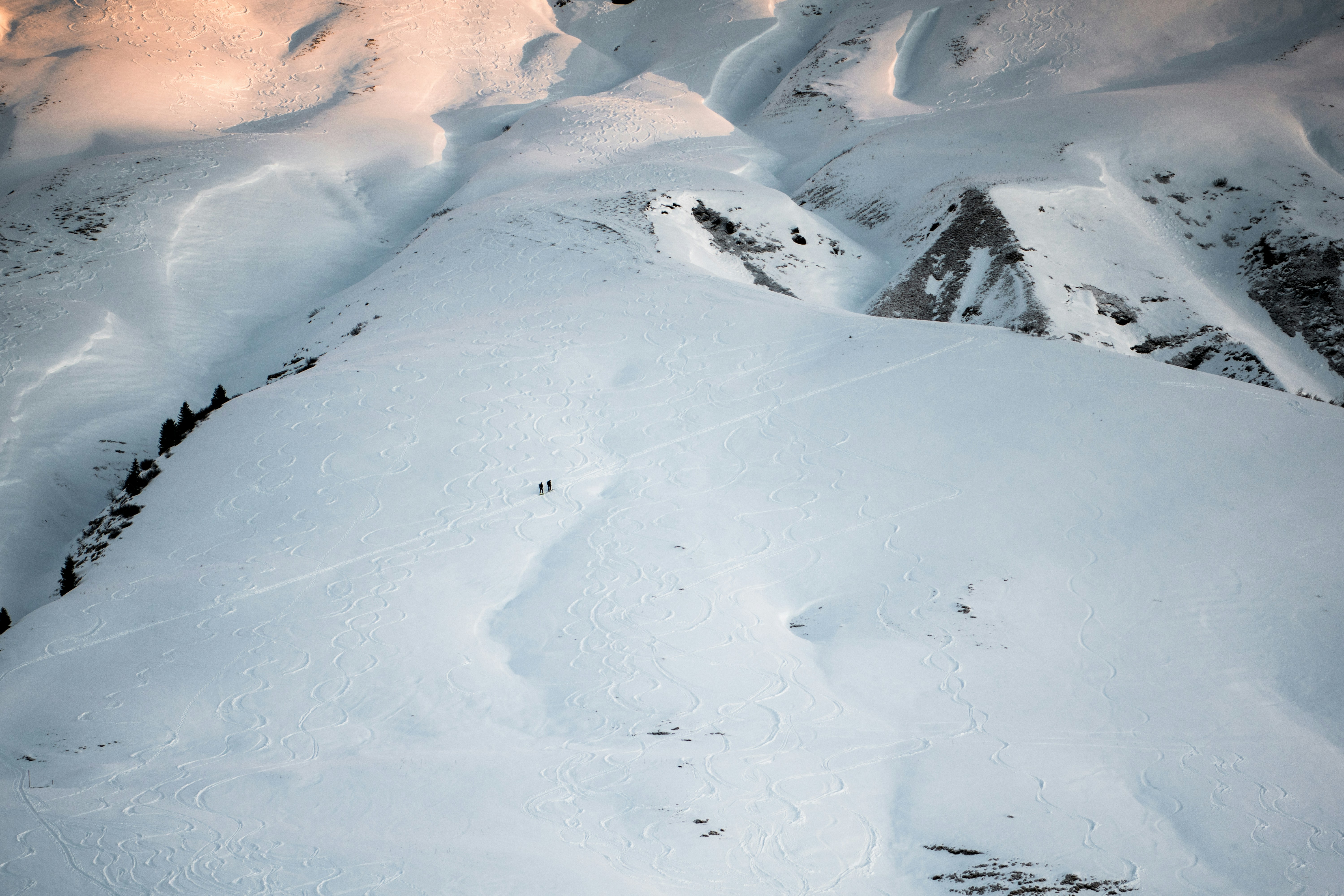Two skiers on a vast snow-covered mountain slope with winding ski tracks