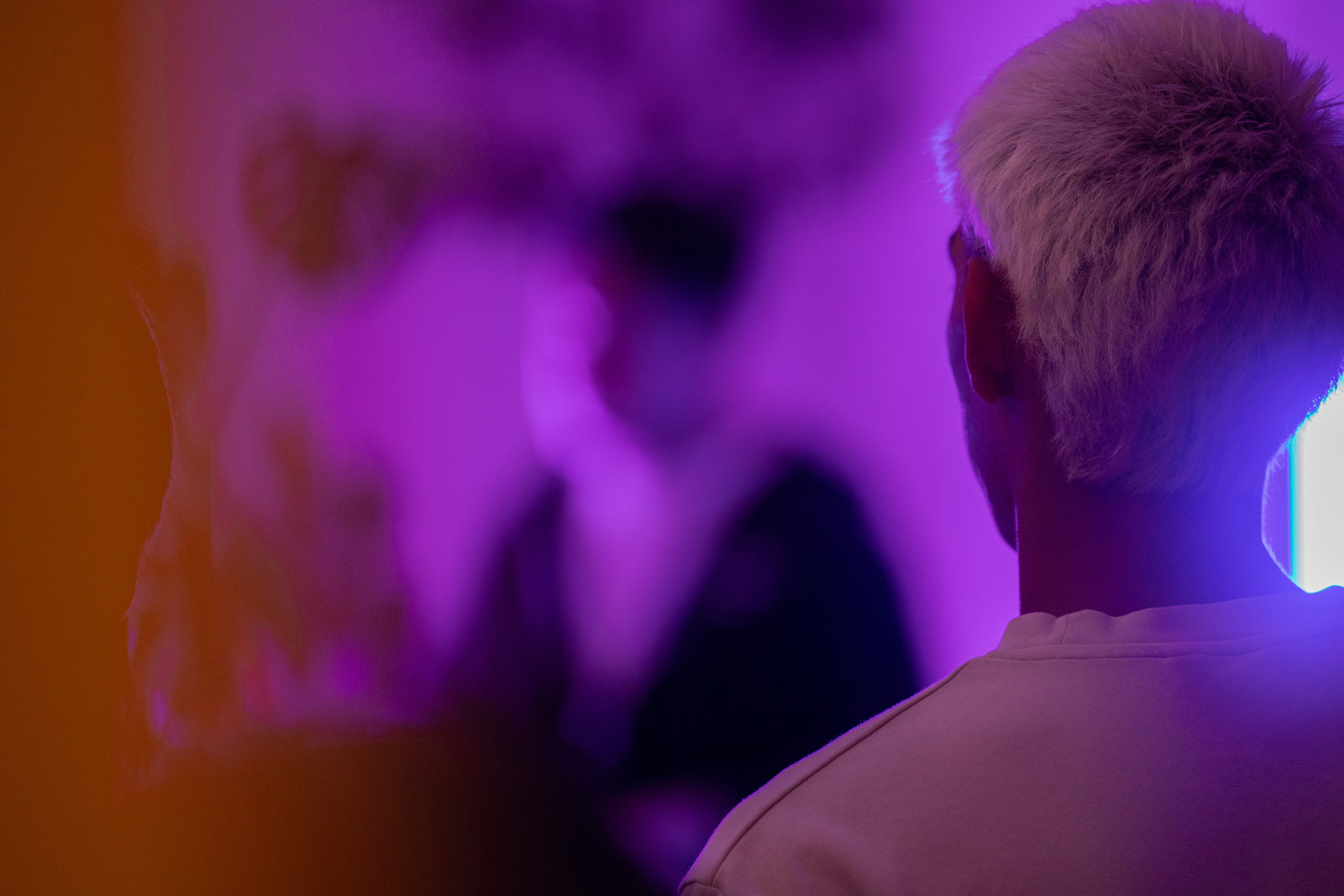 A person with short blonde hair in a white shirt under purple light