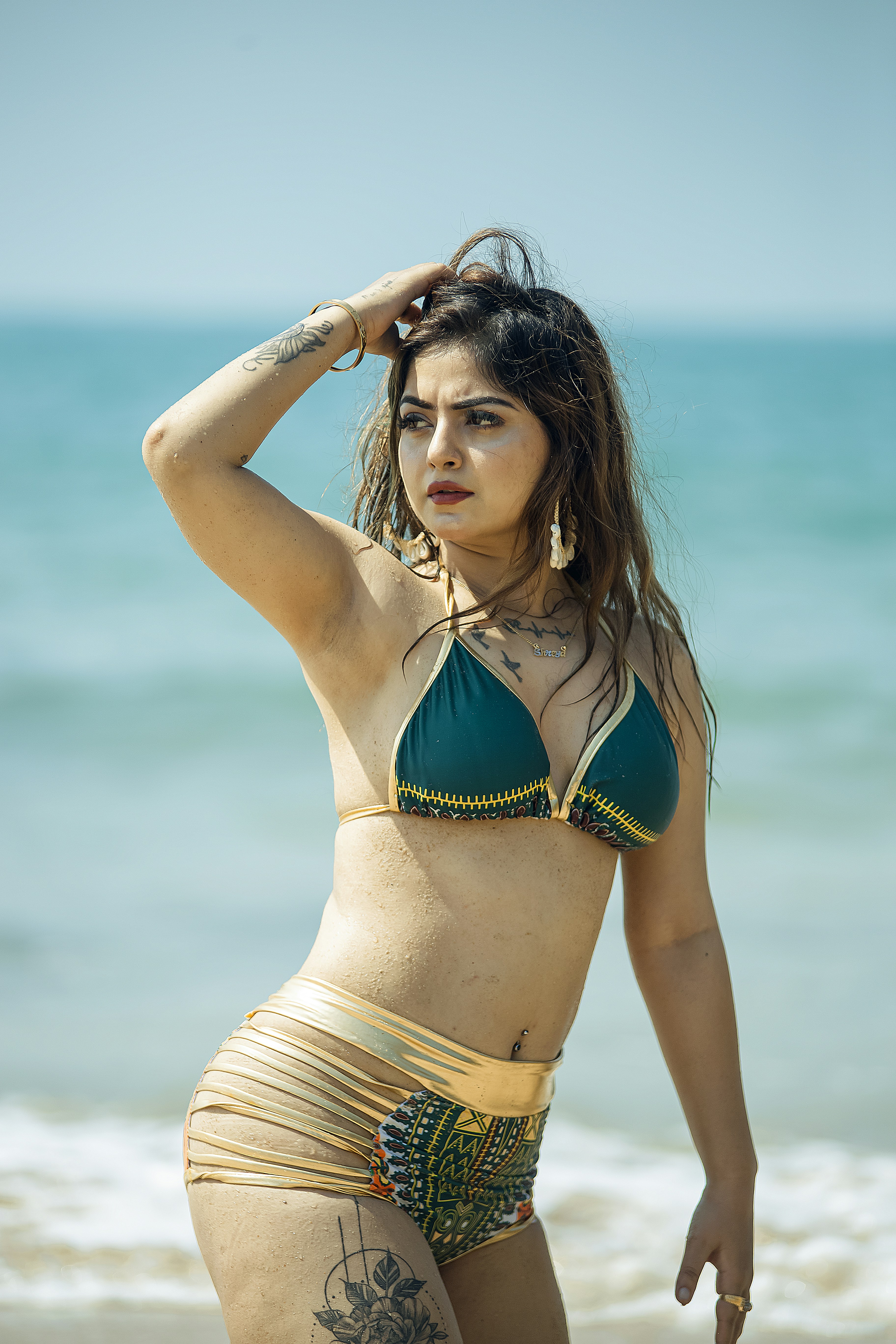 A woman in a patterned green and gold bikini on a sunny beach