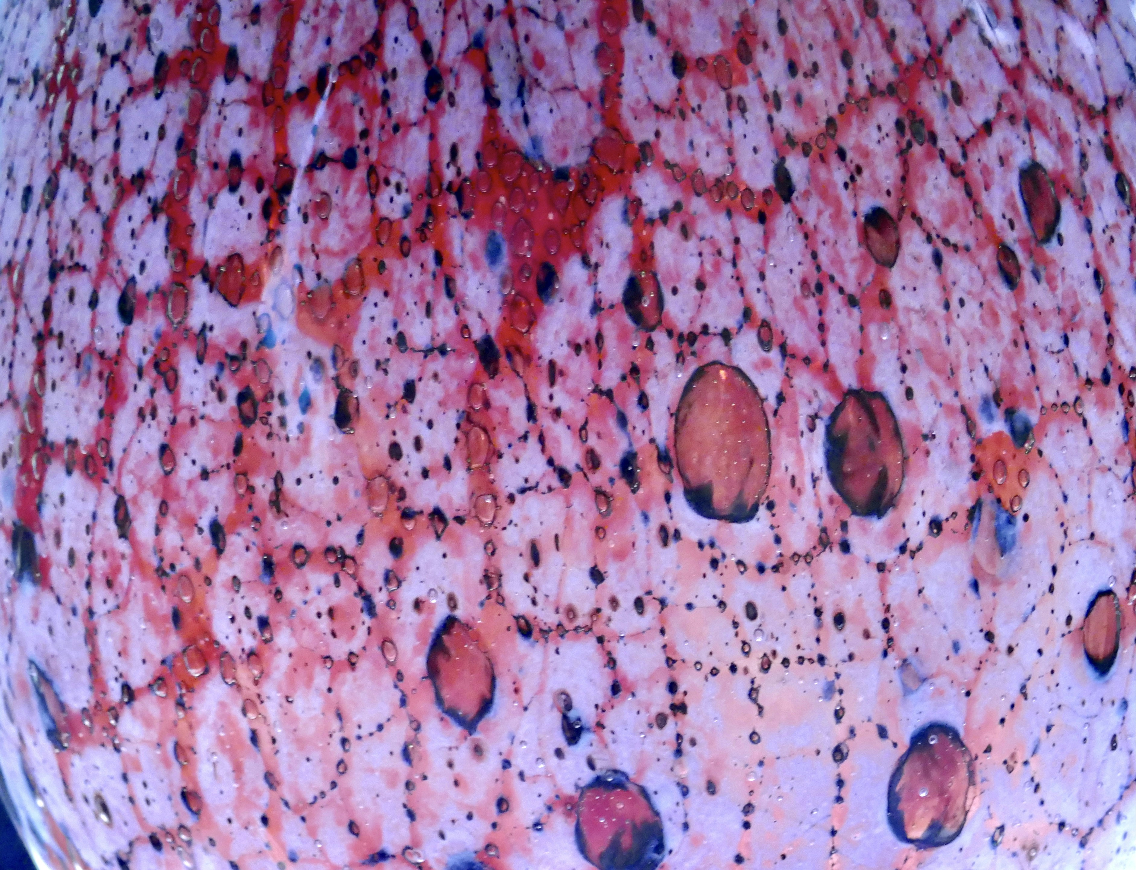 A close-up of textured glass with red and black spots and bubbles