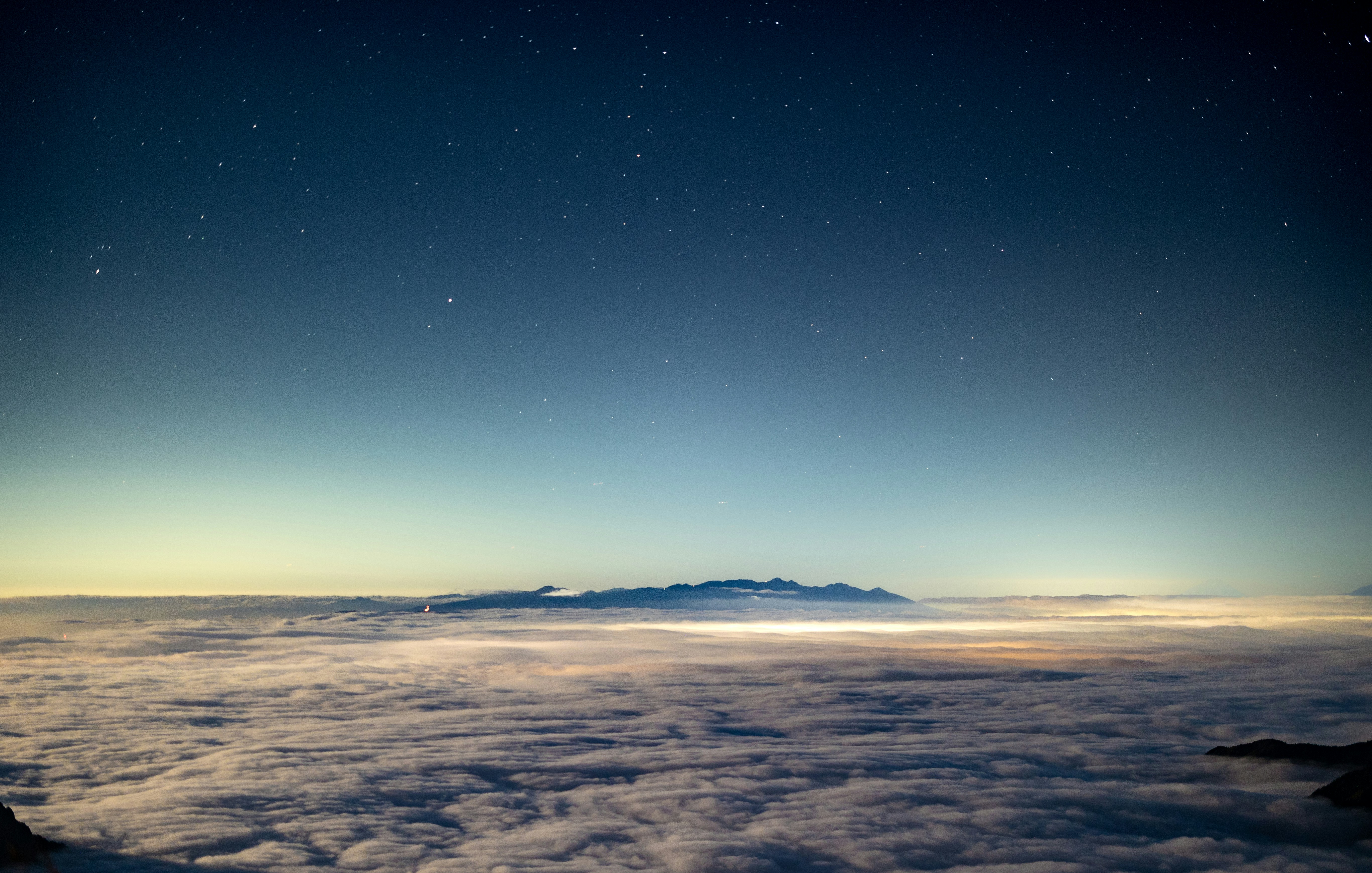 A sea of clouds beneath a starry night sky with distant mountain silhouettes