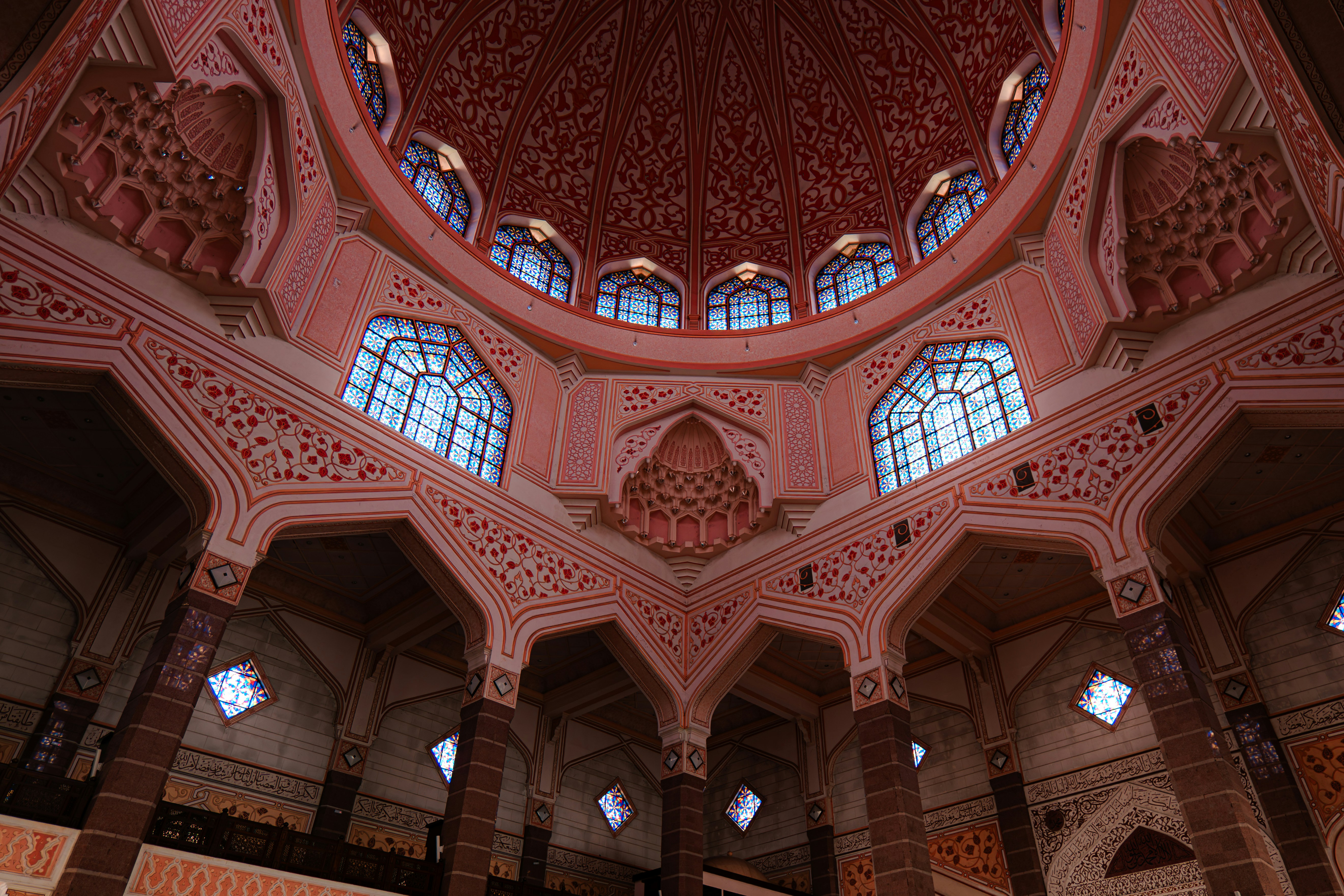 Intricate pink and white geometric patterns inside a large domed mosque interior