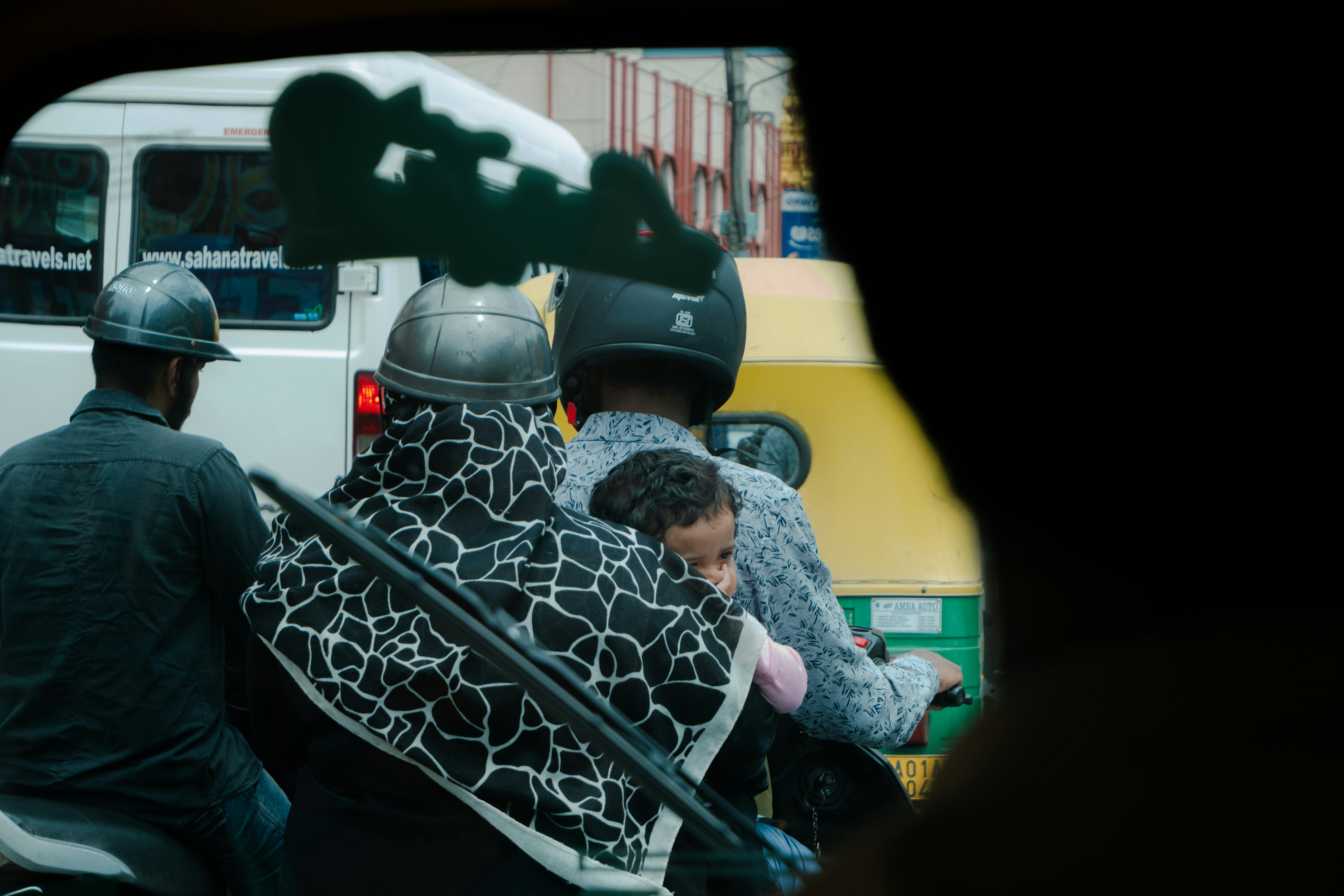 People on motorcycles in traffic with a child and a yellow auto rickshaw