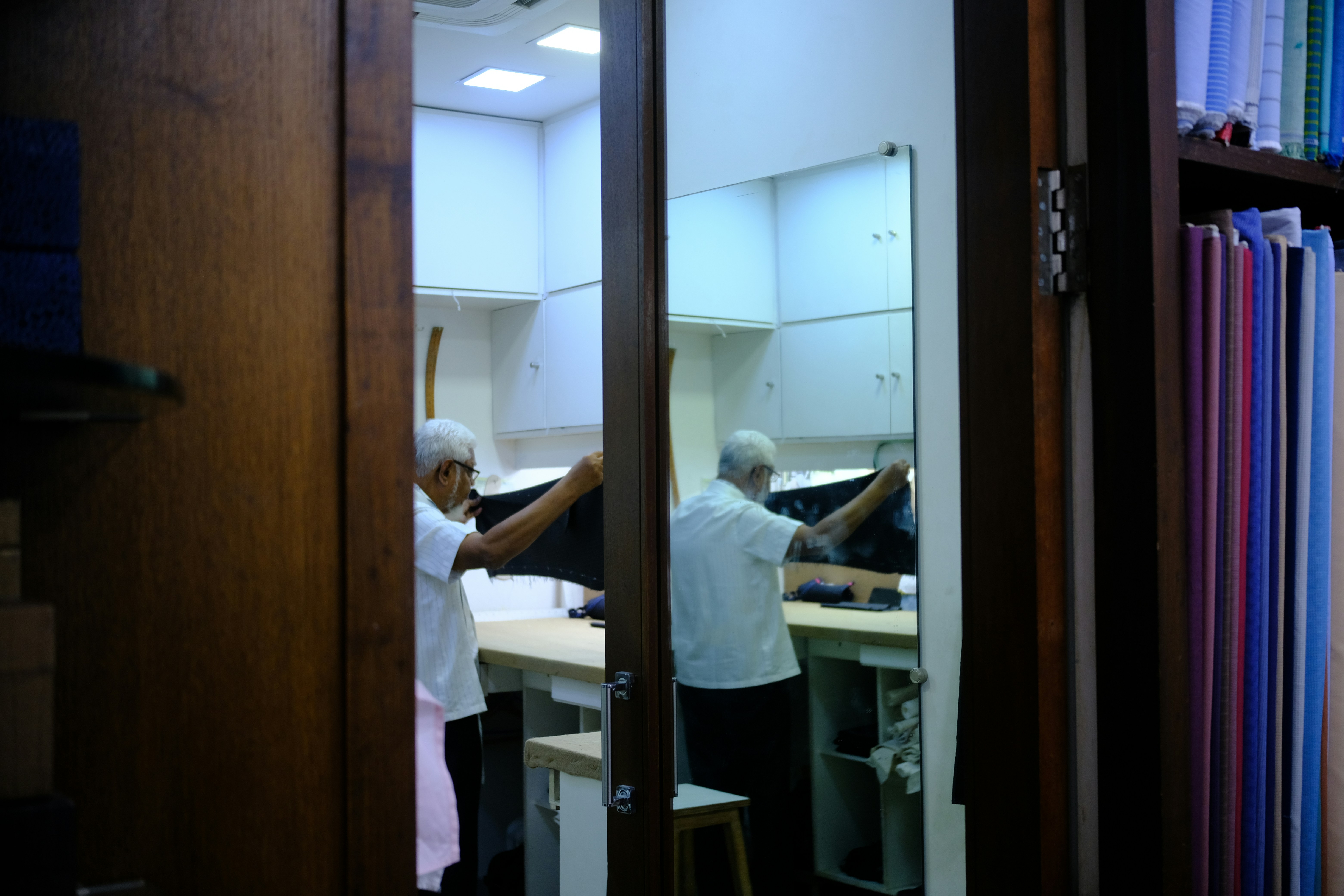 A tailor holding black fabric in a workshop reflected in a tall mirror