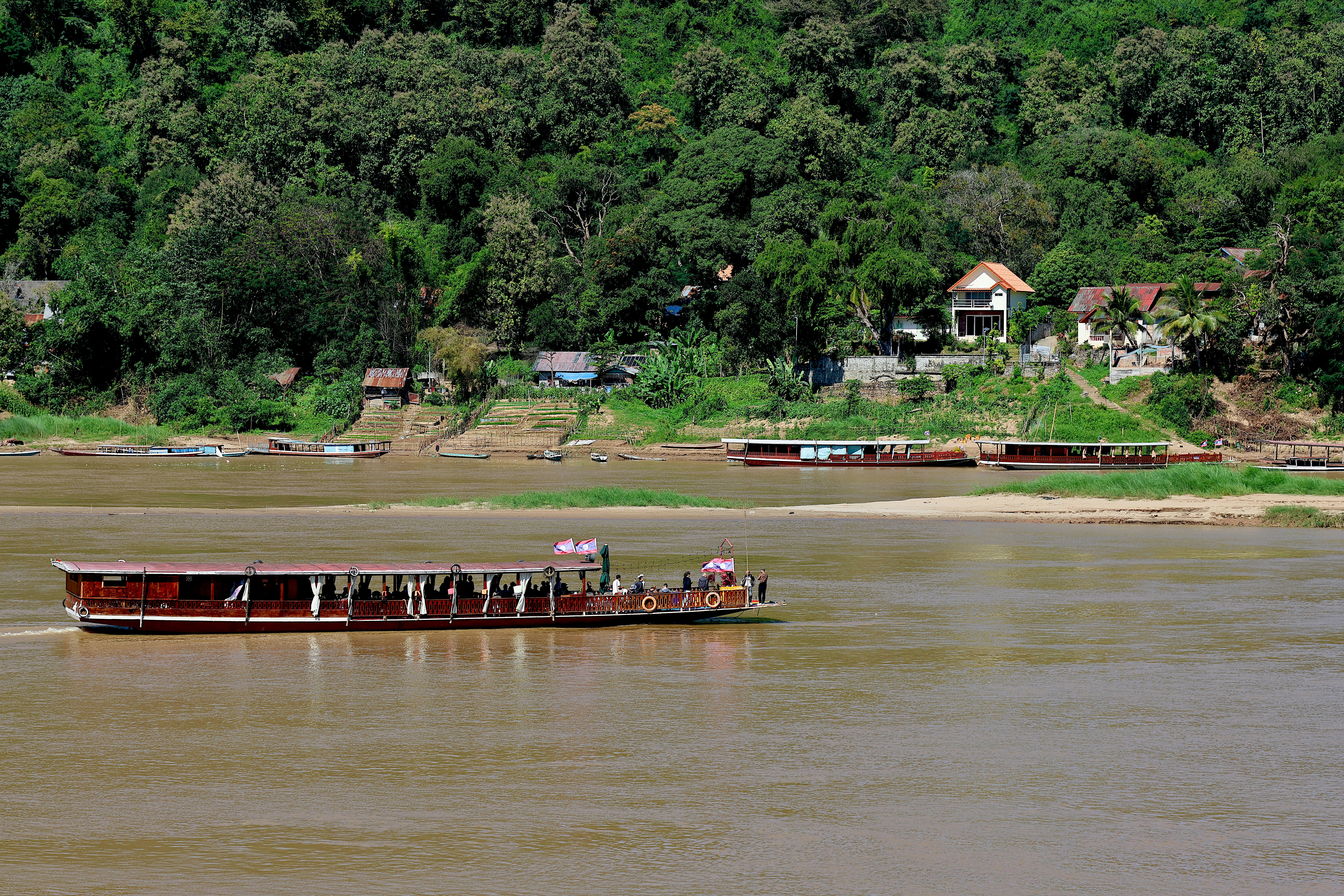 A long wooden boat carrying passengers on the brown Mekong River near Luang Prabang