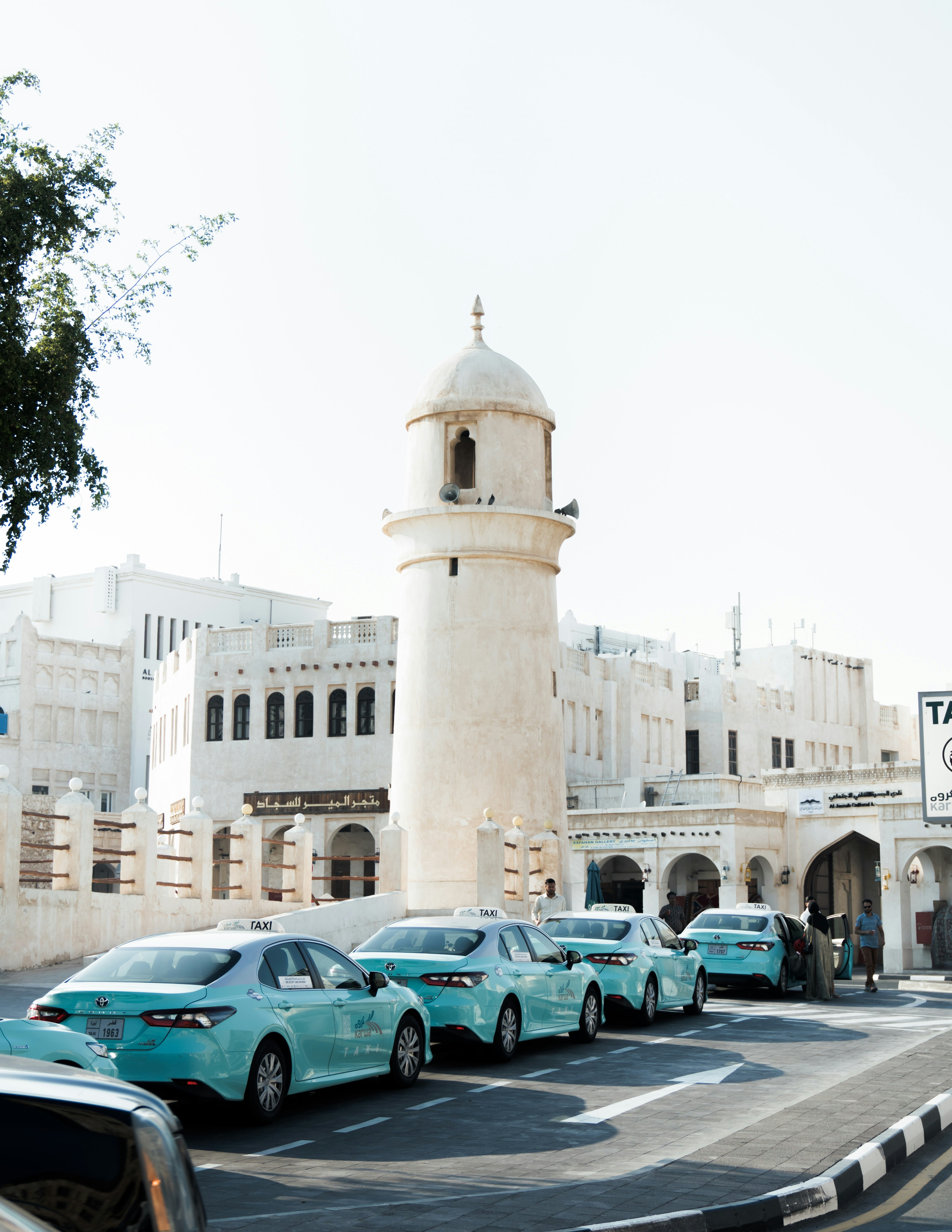 Una fila de taxis turquesa estacionados cerca de un minarete blanco en Souq Waqif