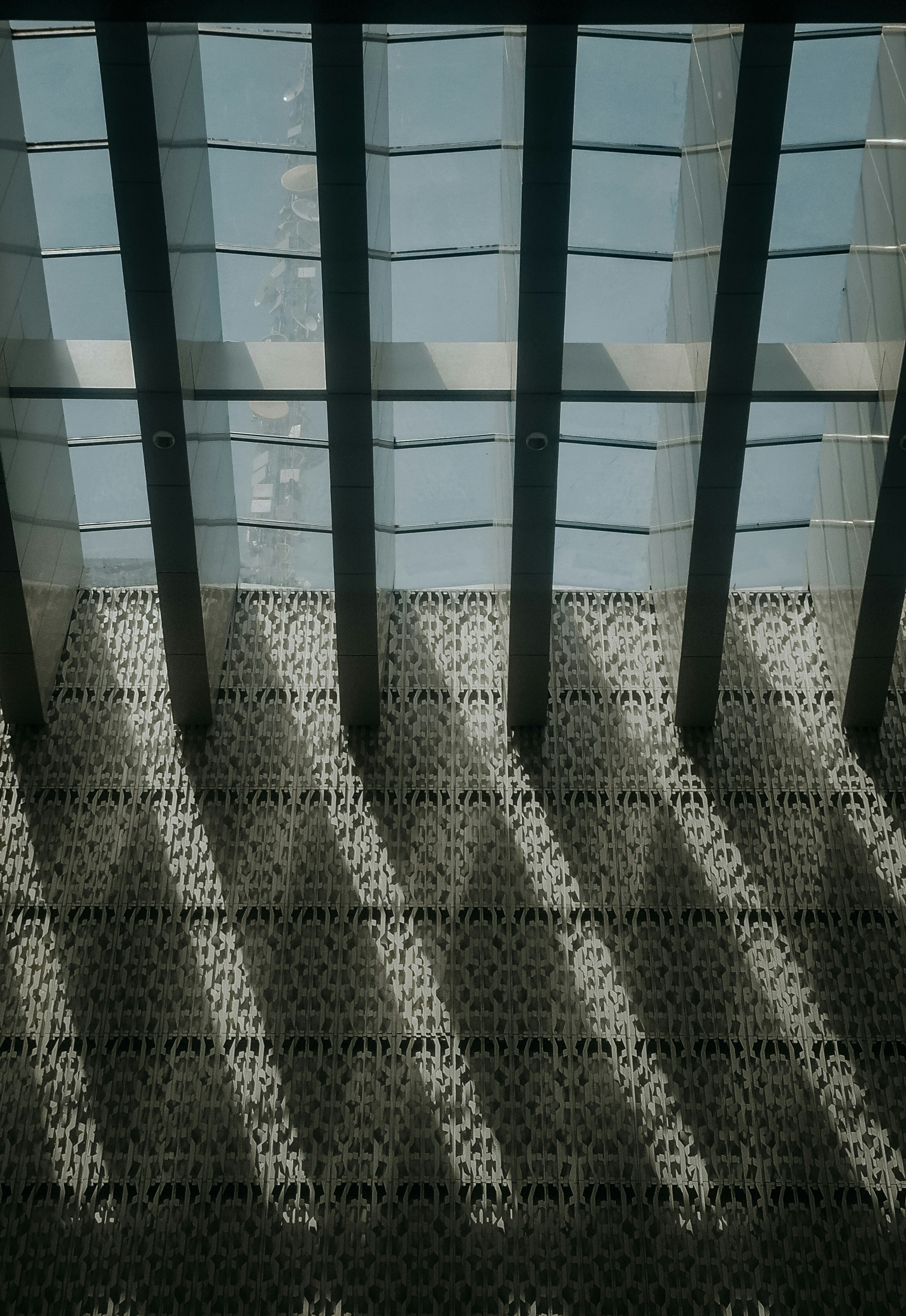 Sunlight casting long shadows through a glass ceiling onto an intricate patterned wall