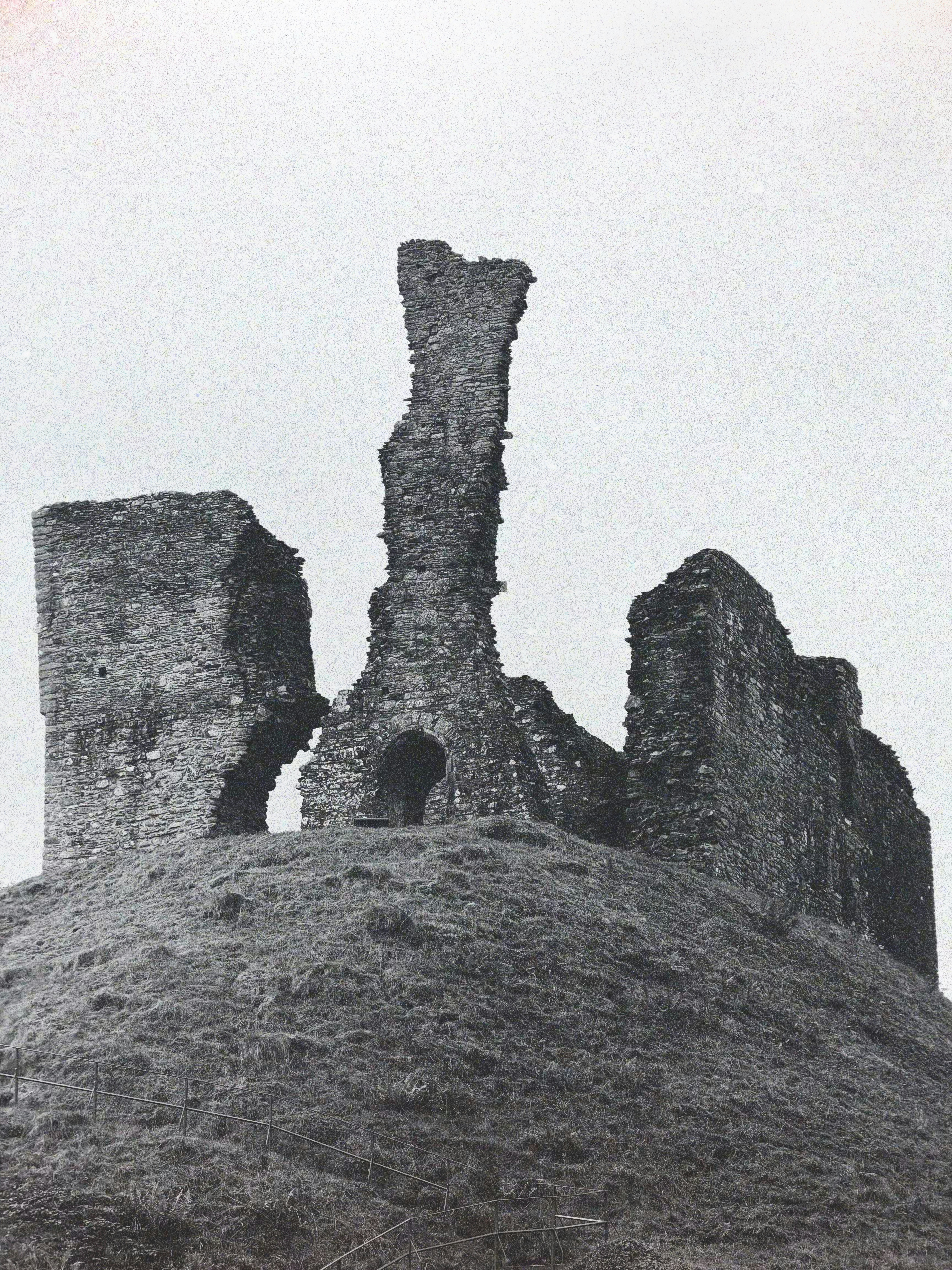 Stone ruins of a castle on a grassy hill under a pale sky