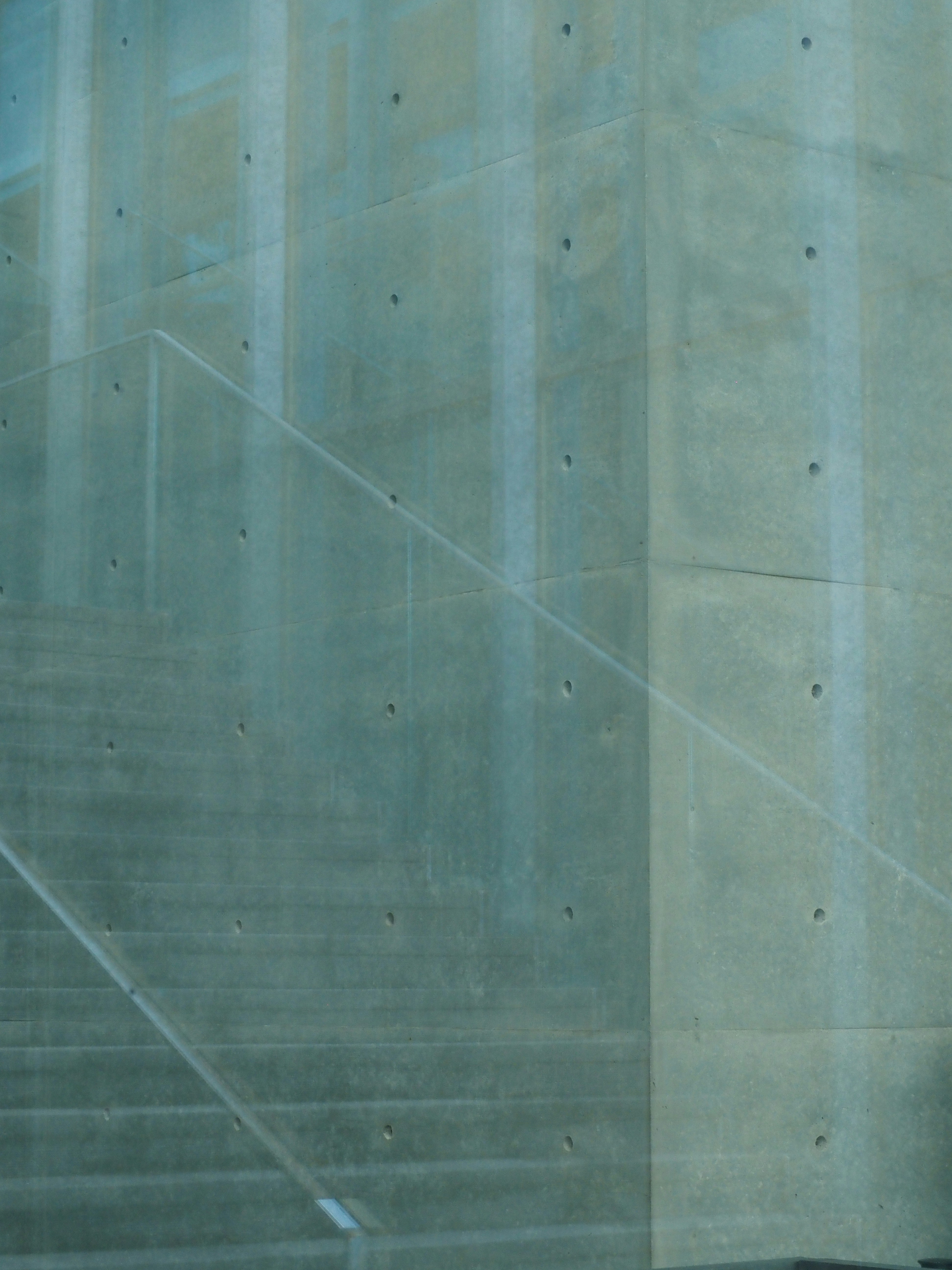 A glass railing in front of a smooth concrete wall with circular indentations