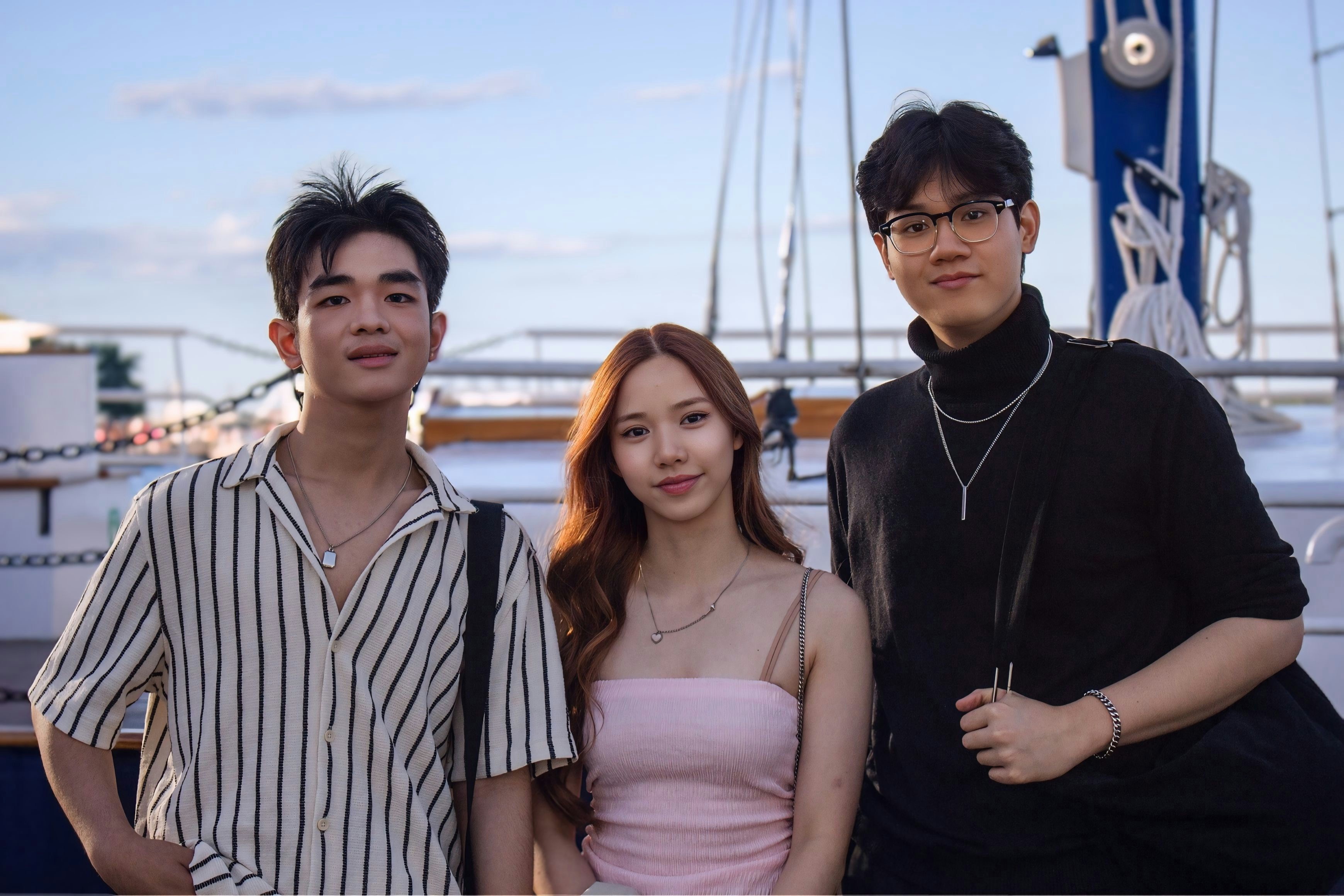 Three young adults standing together on a boat deck under a clear blue sky