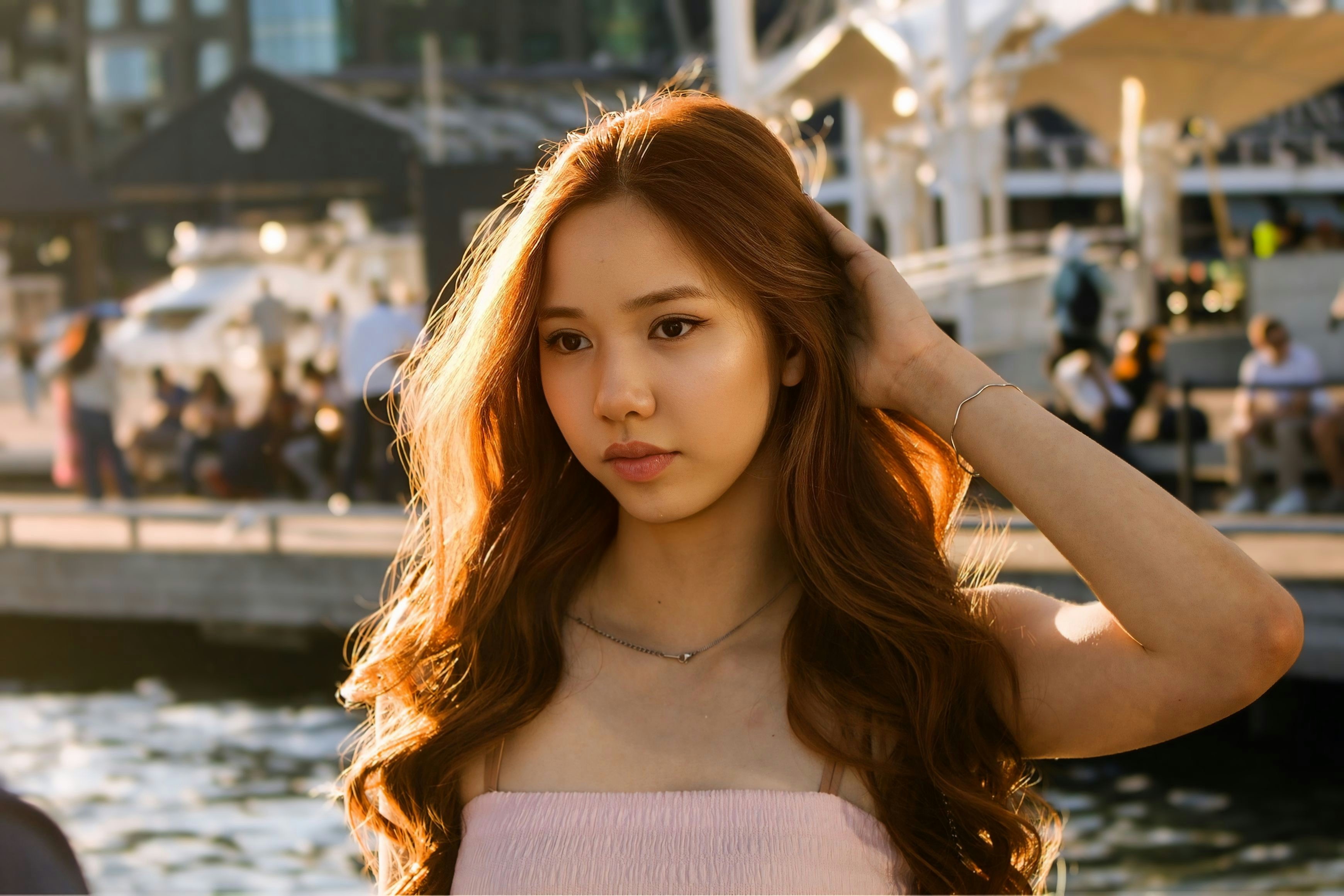 A woman with long brown hair touching her hair by a waterfront at golden hour