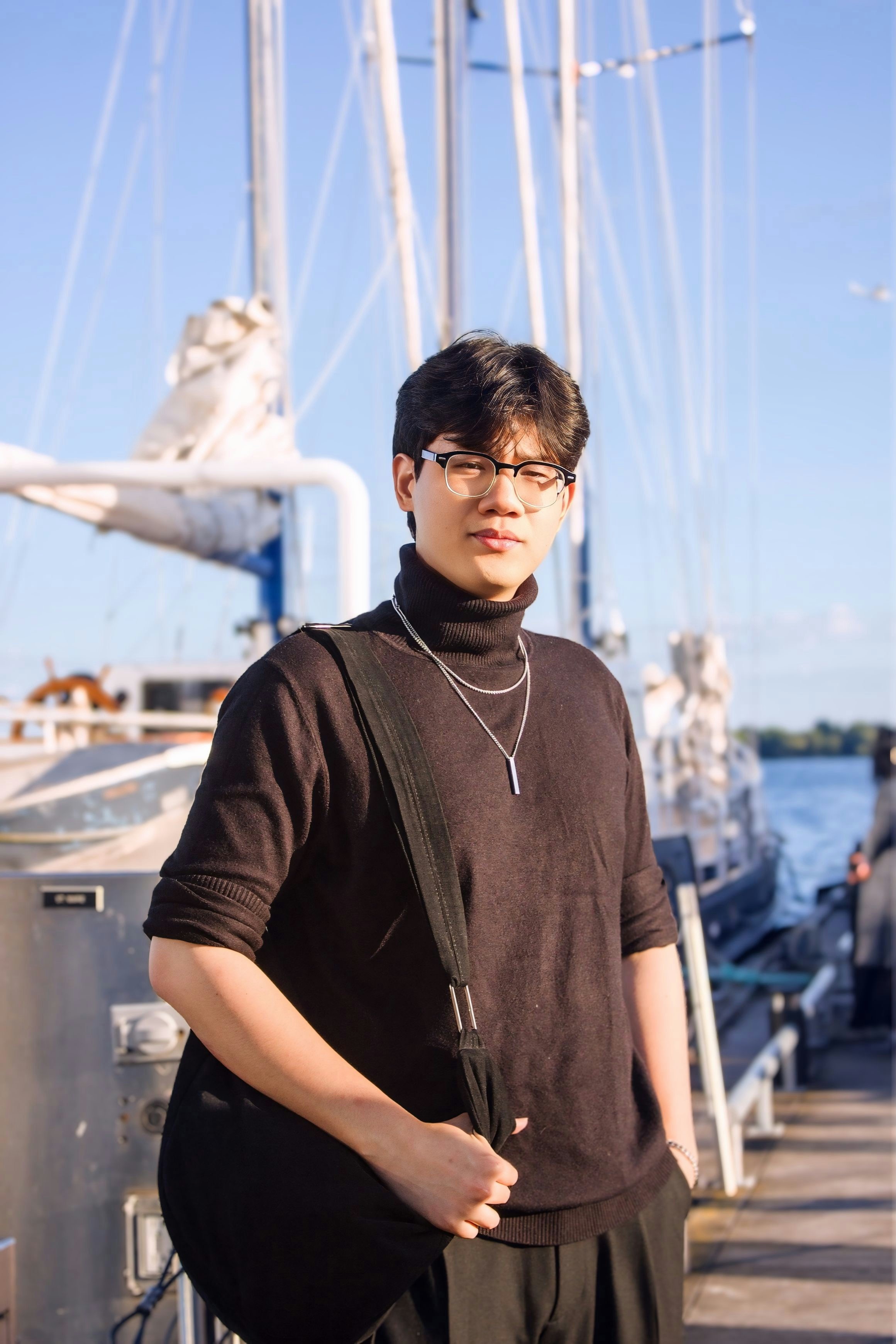 A young man in a black turtleneck and glasses on a boat dock